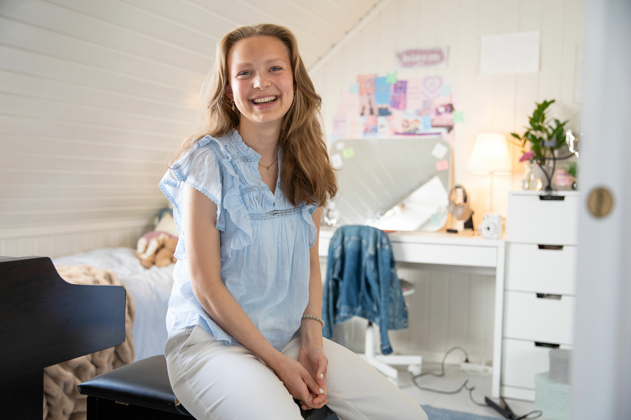 Tenåringsjente sitter på pianokrakken inne på det lyse pikerommet. I bakgrunnen står både piano, seng og pult.