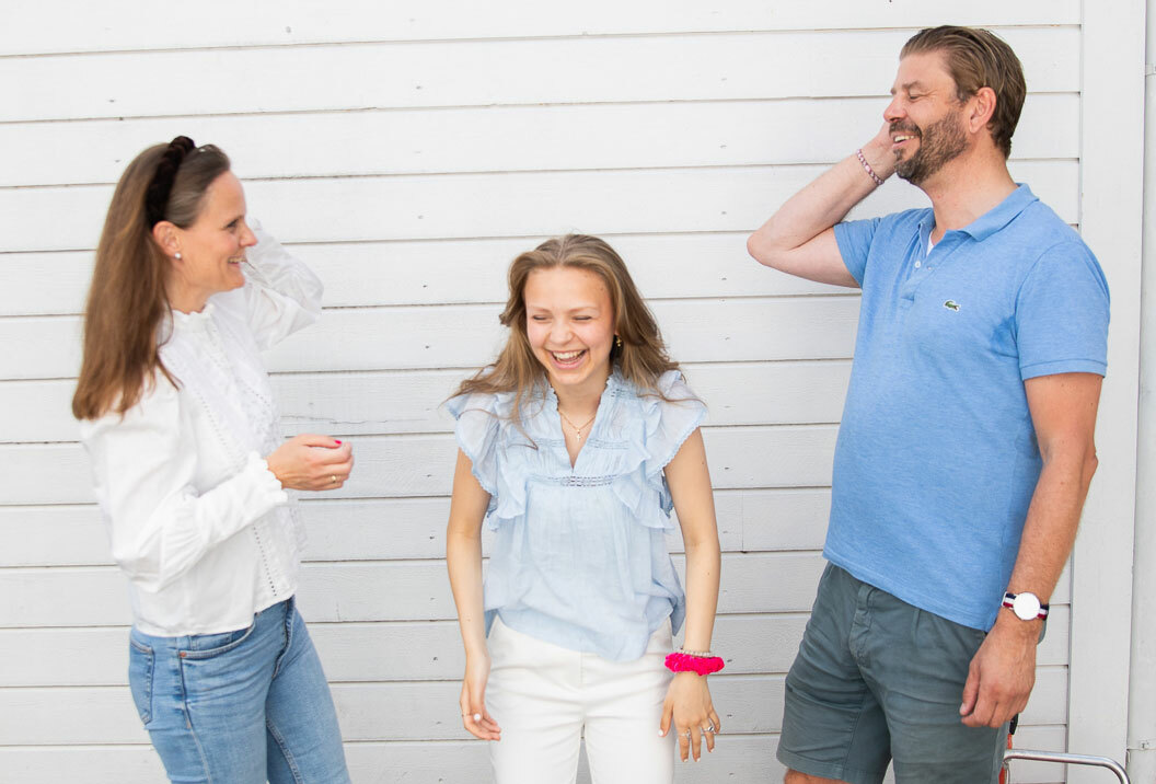 Mor og far på hver siden av en tenåringsdatter. Alle ler.