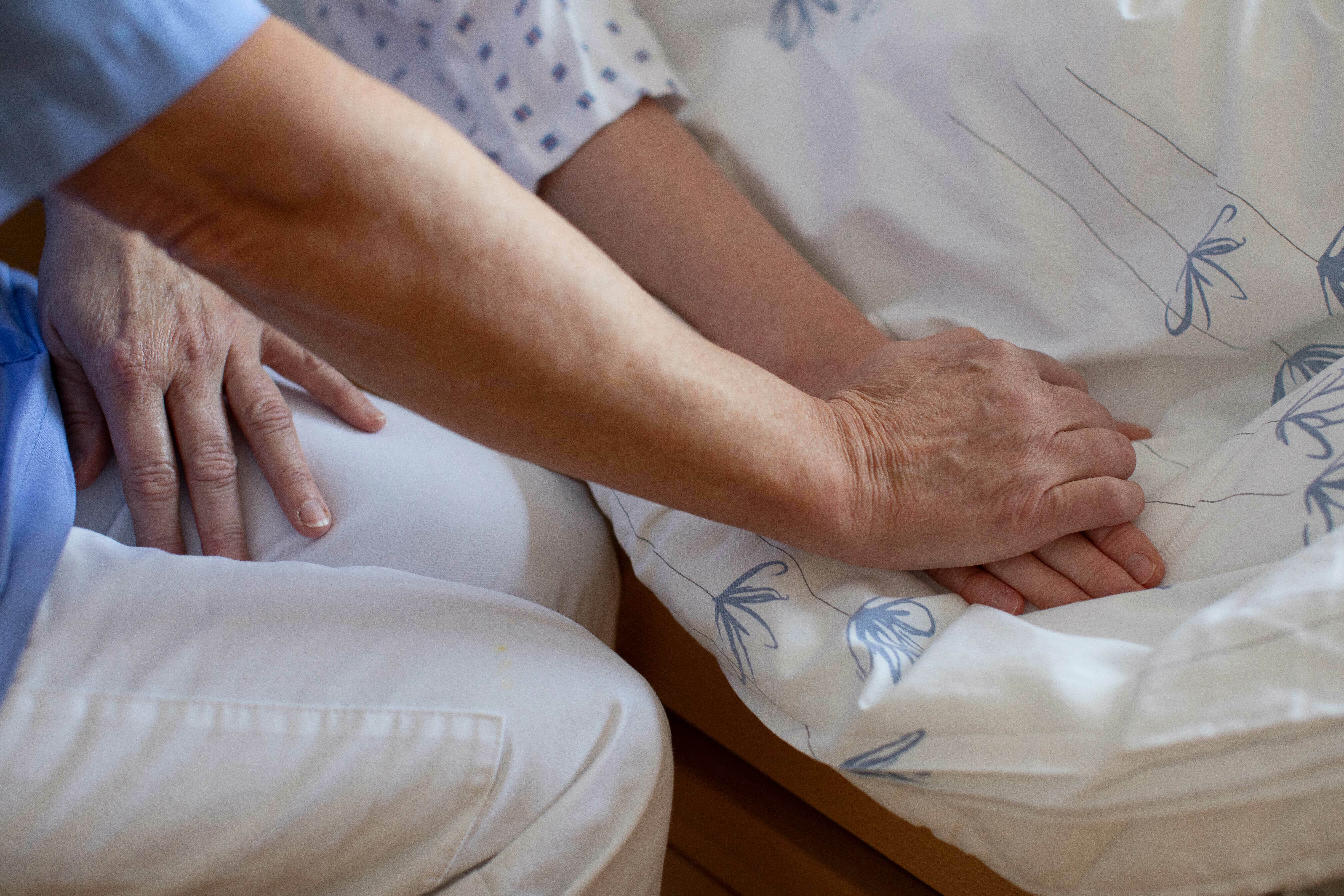 En sykepleiers hånd som holder pasientens hånd på en dyne.