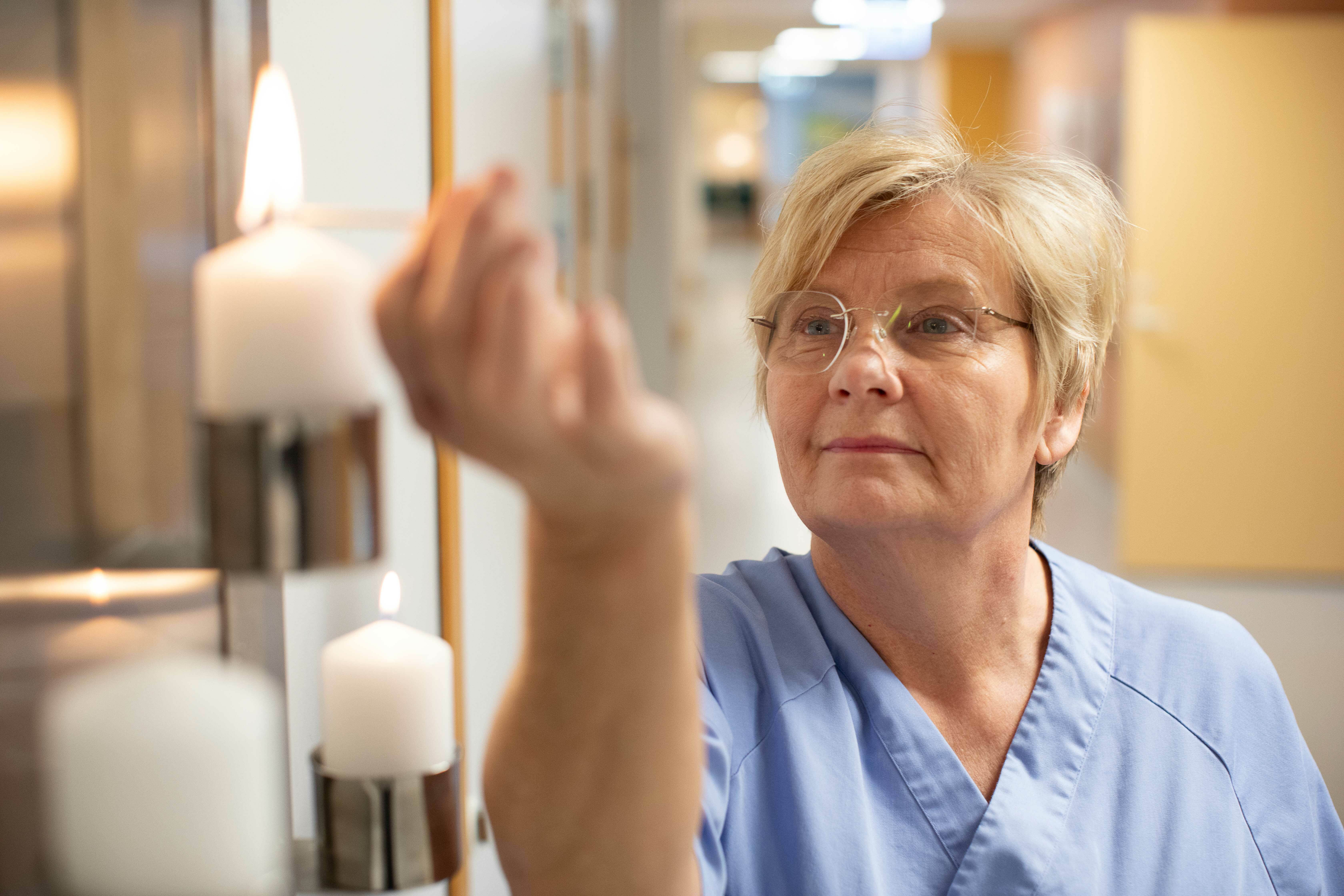 Endre kvinne med lyseblå sykepleier uniform tenner et lys