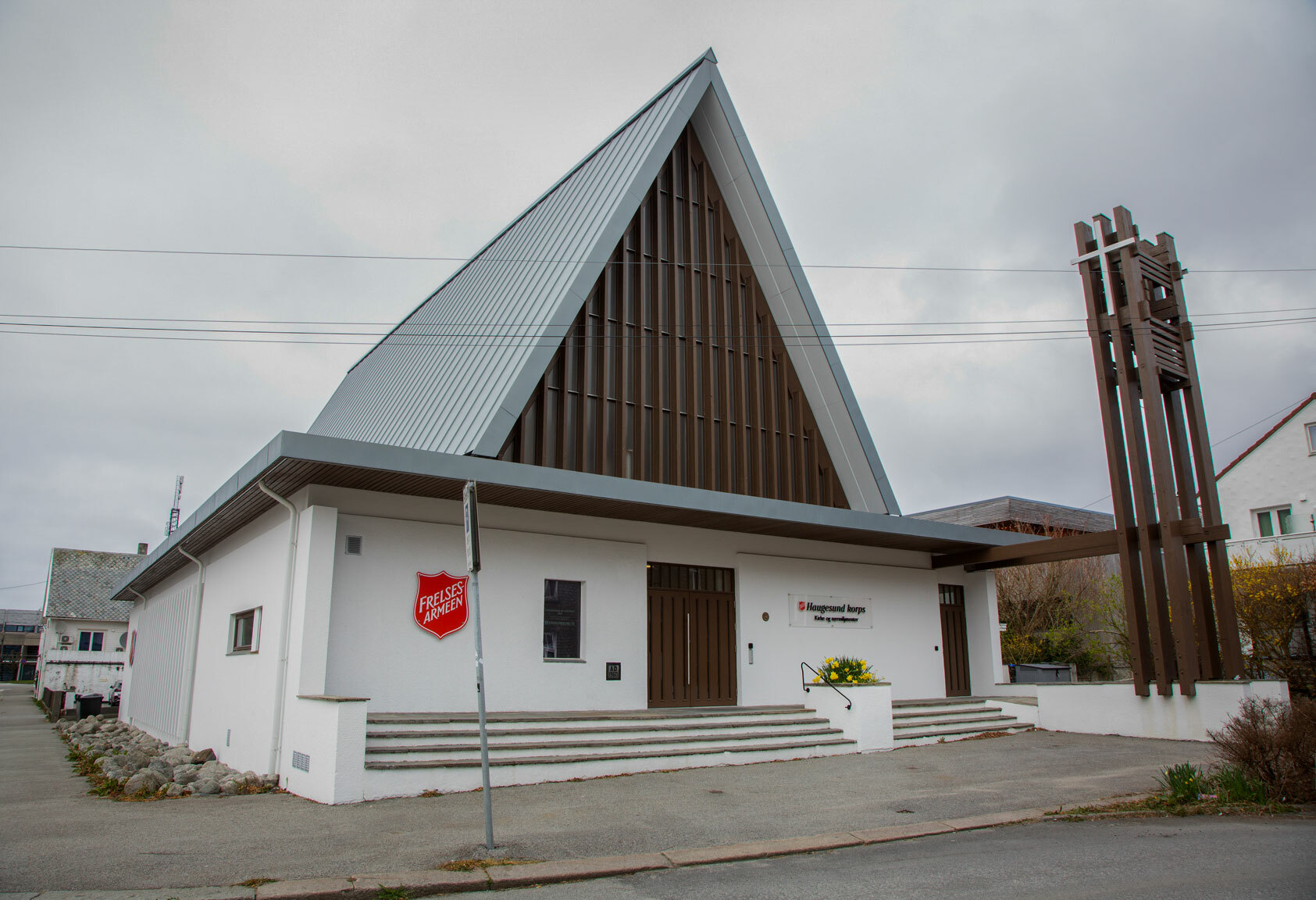 Foto: Eksteriør av kirke i moderne stil. Hvitt murbygg med en spiss oppover i brunt tre.