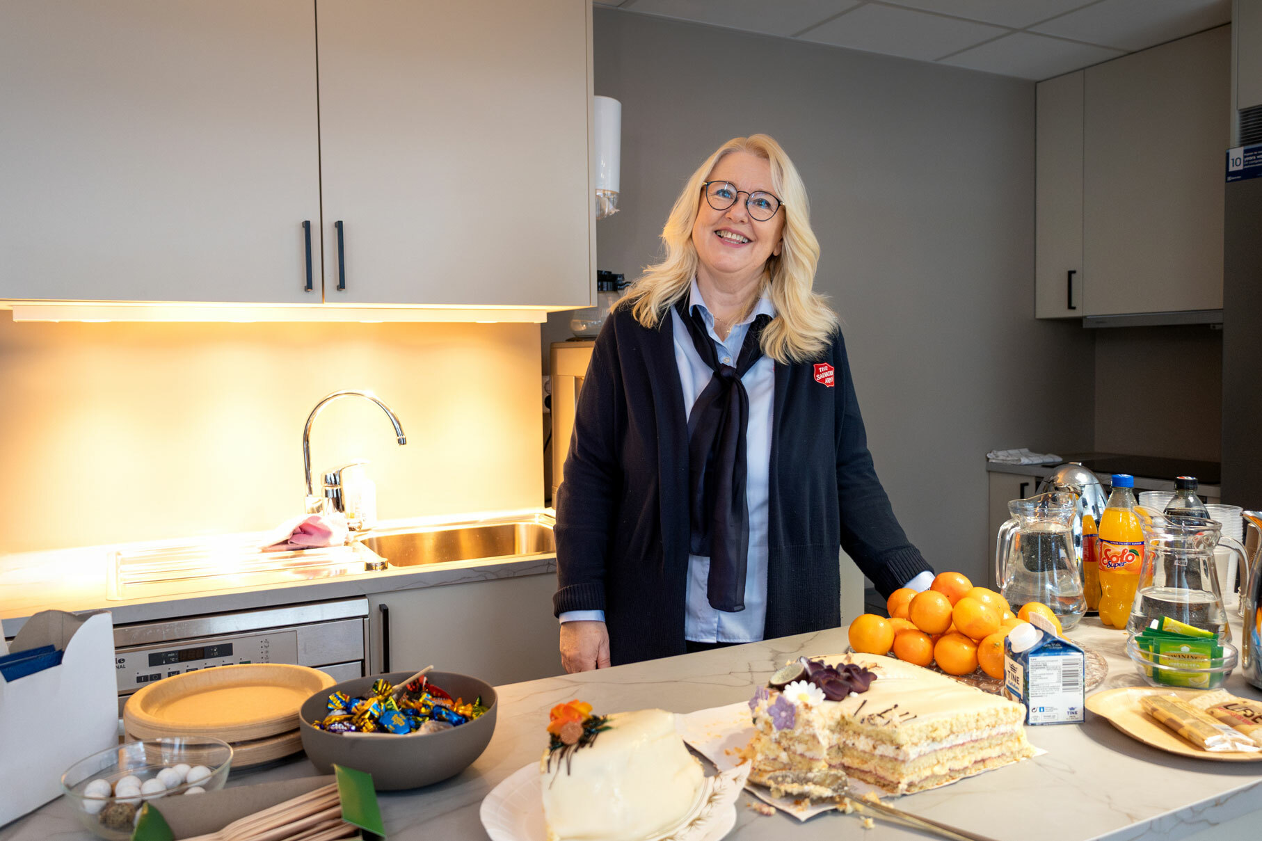 Foto: Kvinne med halvlangt, blondt hår og briller smiler fra et moderne kjøkken.