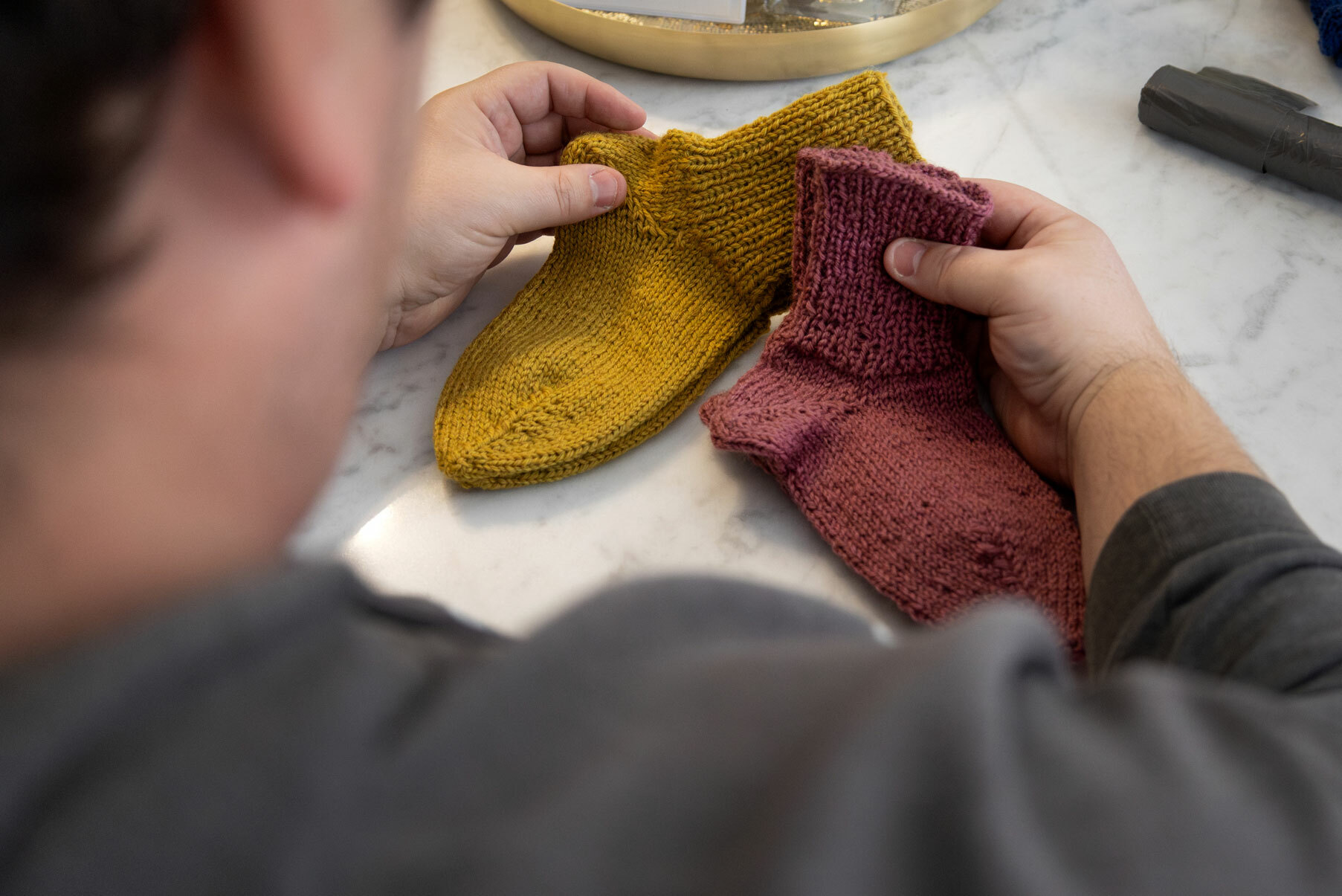 Foto: Mann holder i to ulike farger med strikkesokker i ull. Han har ryggen tl kamera, så vi ser bare litt av nakken og ene siden av ansiktet.