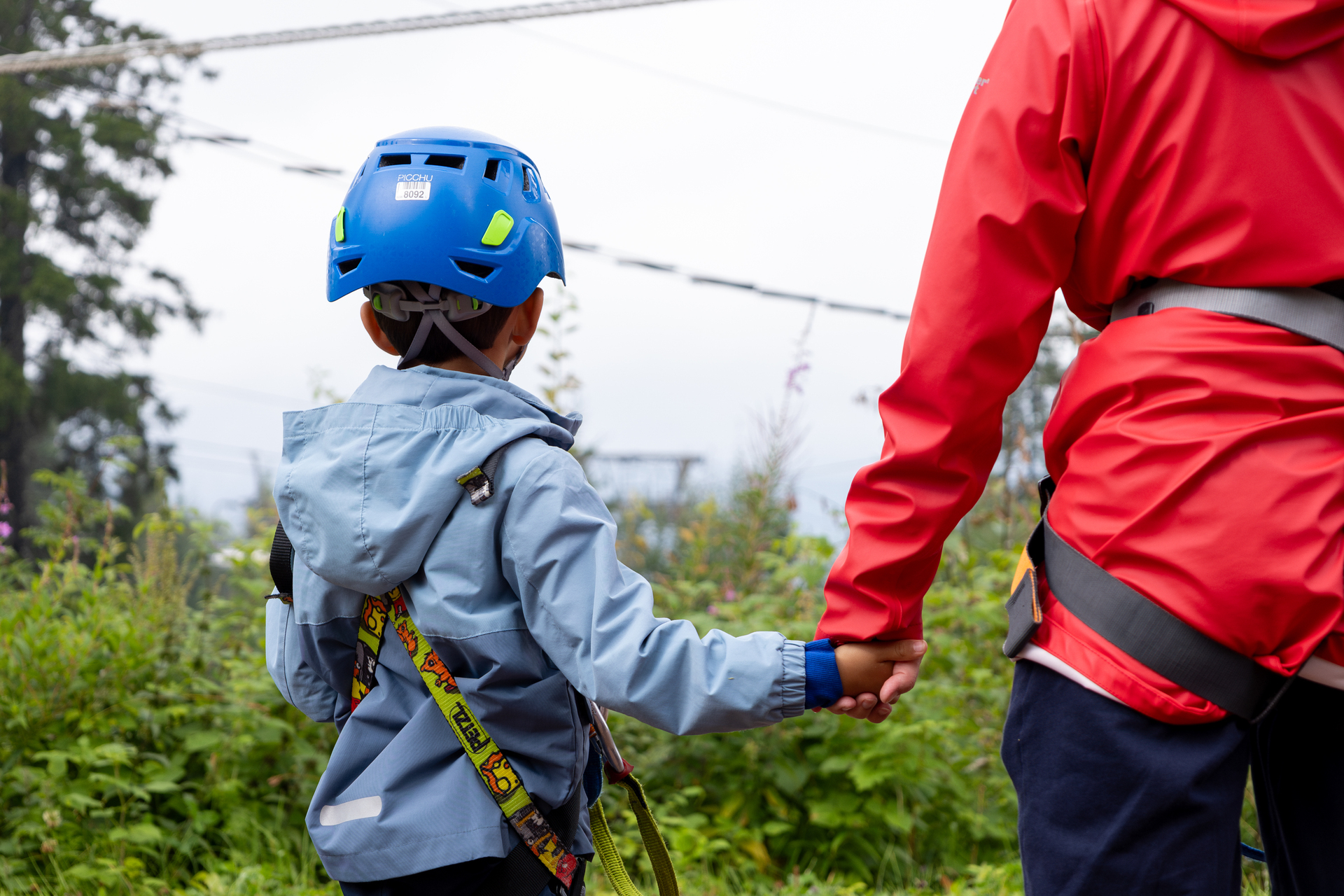 To foto etter hverandre: Det første viser en liten gutt som får på seg klatresele og det andre samme gutt som holder moren sin i hånda mens de skuer utover skog og stålvaiere.