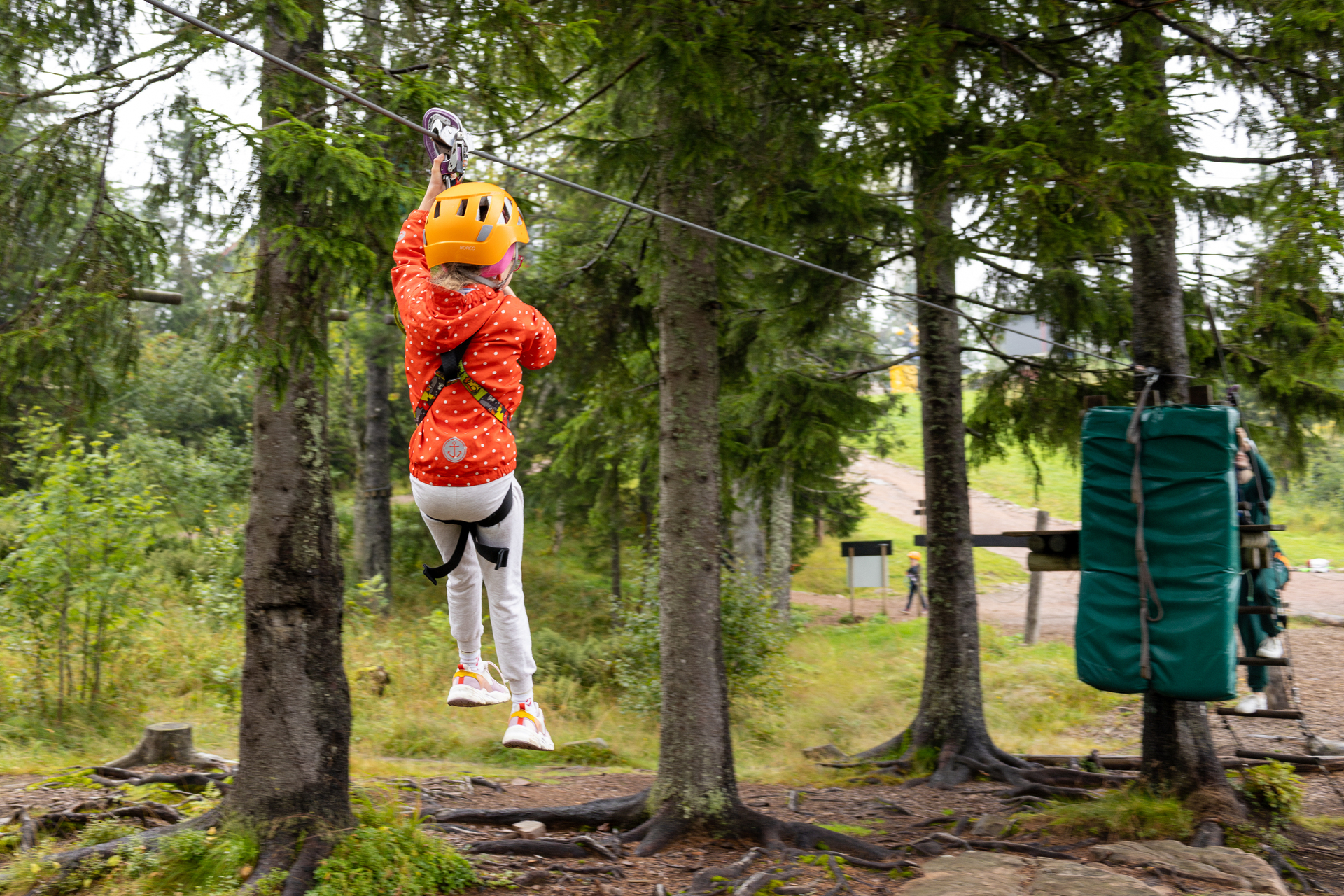 To foto etter hverandre: Jente med hjelm og briller som fester en karabin. Samme jente som glir gjennom lufta fre et tre til et annet.