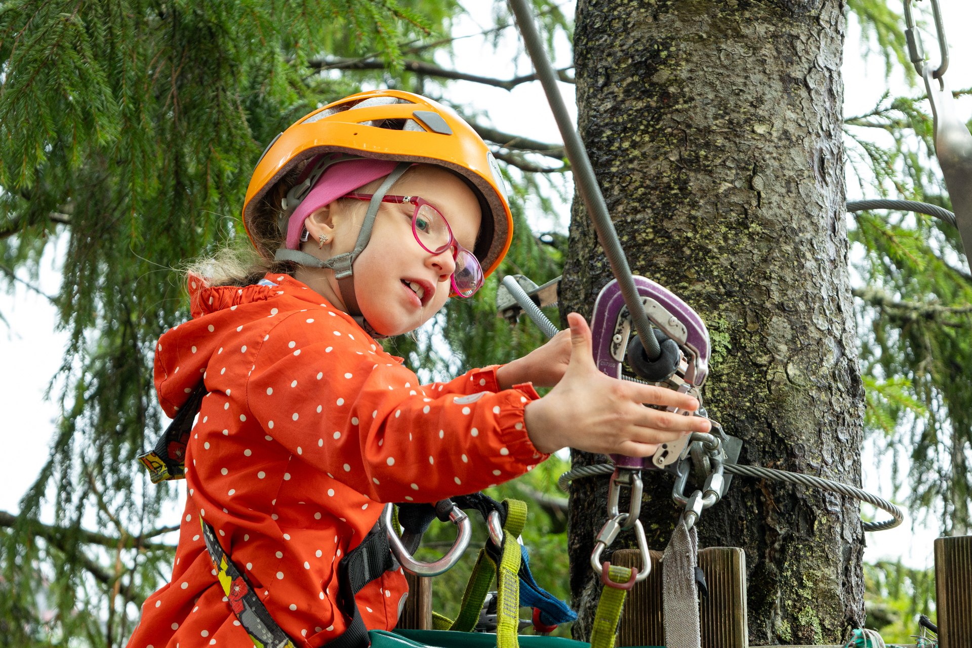 To foto etter hverandre: Jente med hjelm og briller som fester en karabin. Samme jente som glir gjennom lufta fre et tre til et annet.
