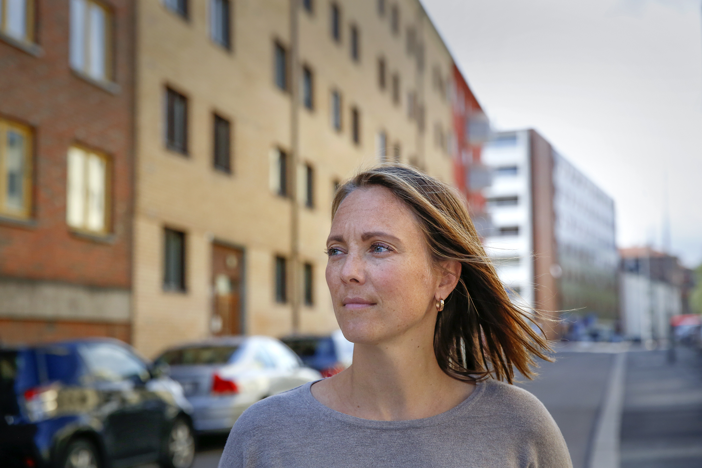 Foto: Kvinne med halvlangt blondt hår utenfor blokk, hun ser mot venstre oppover gata.