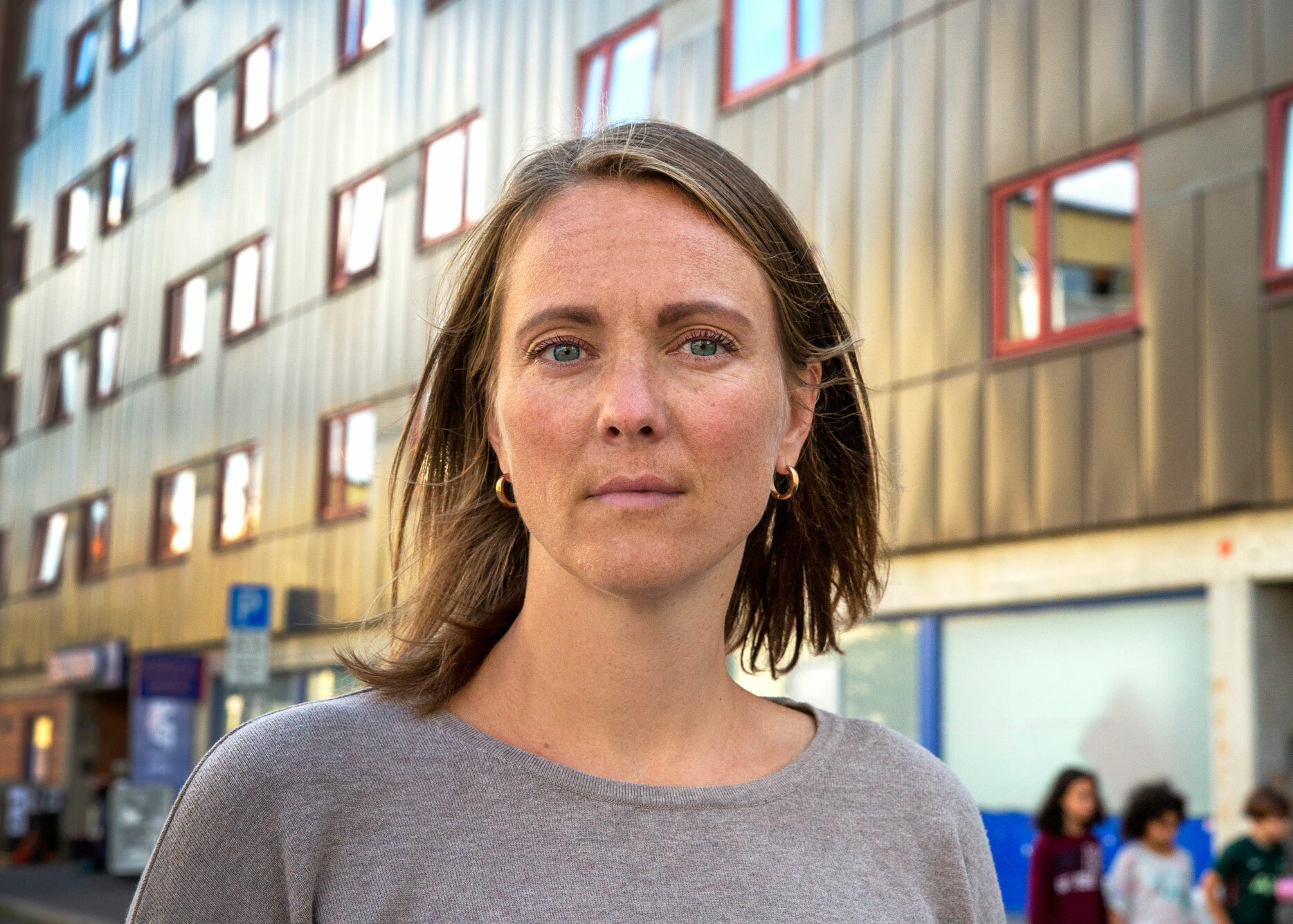 Foto: Kvinne i 40-årene med halvlangt, mørkeblondt hår står foran en stor boligblokk.