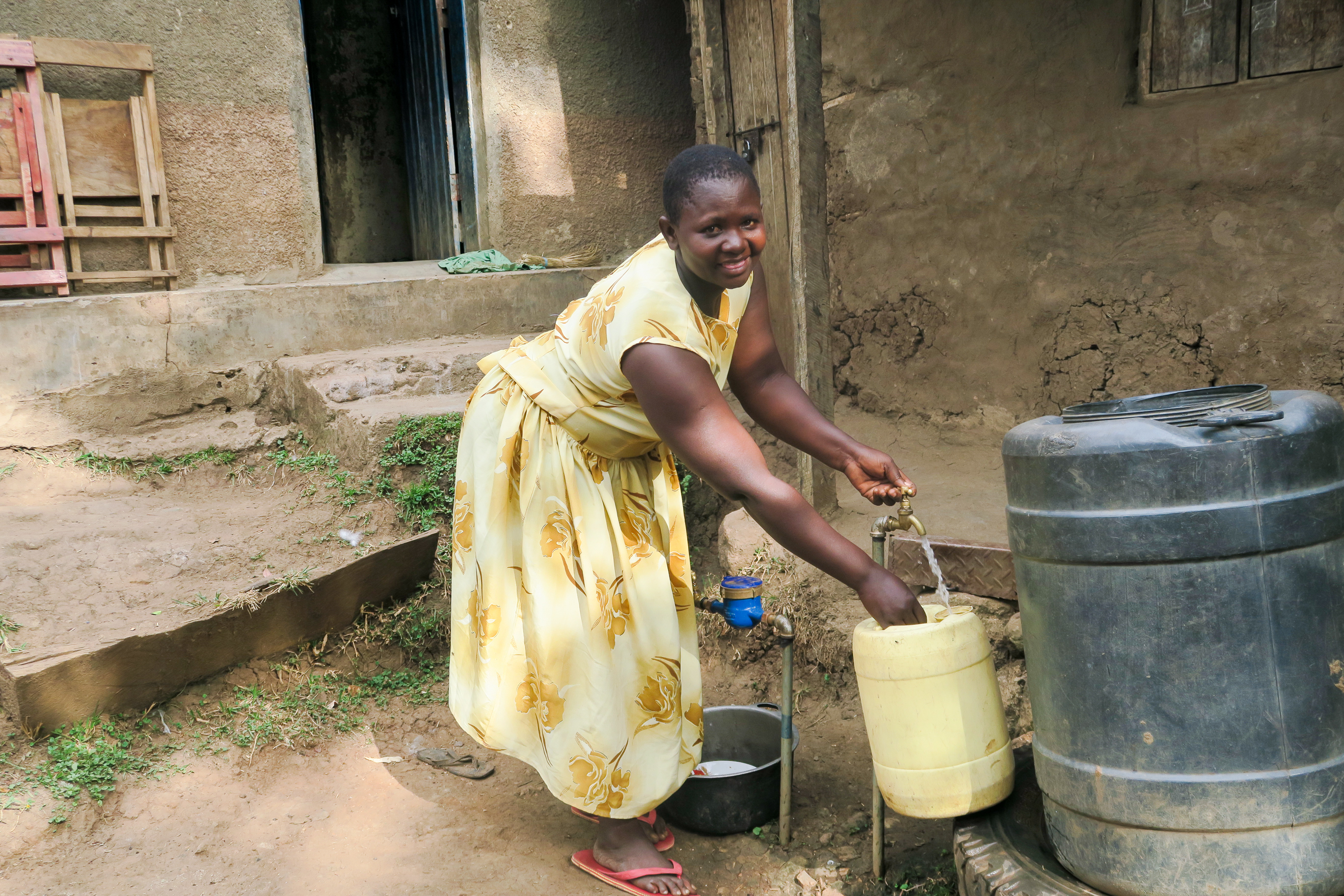 En Afrikansk kvinne fyller rent vann en gul bøtte
