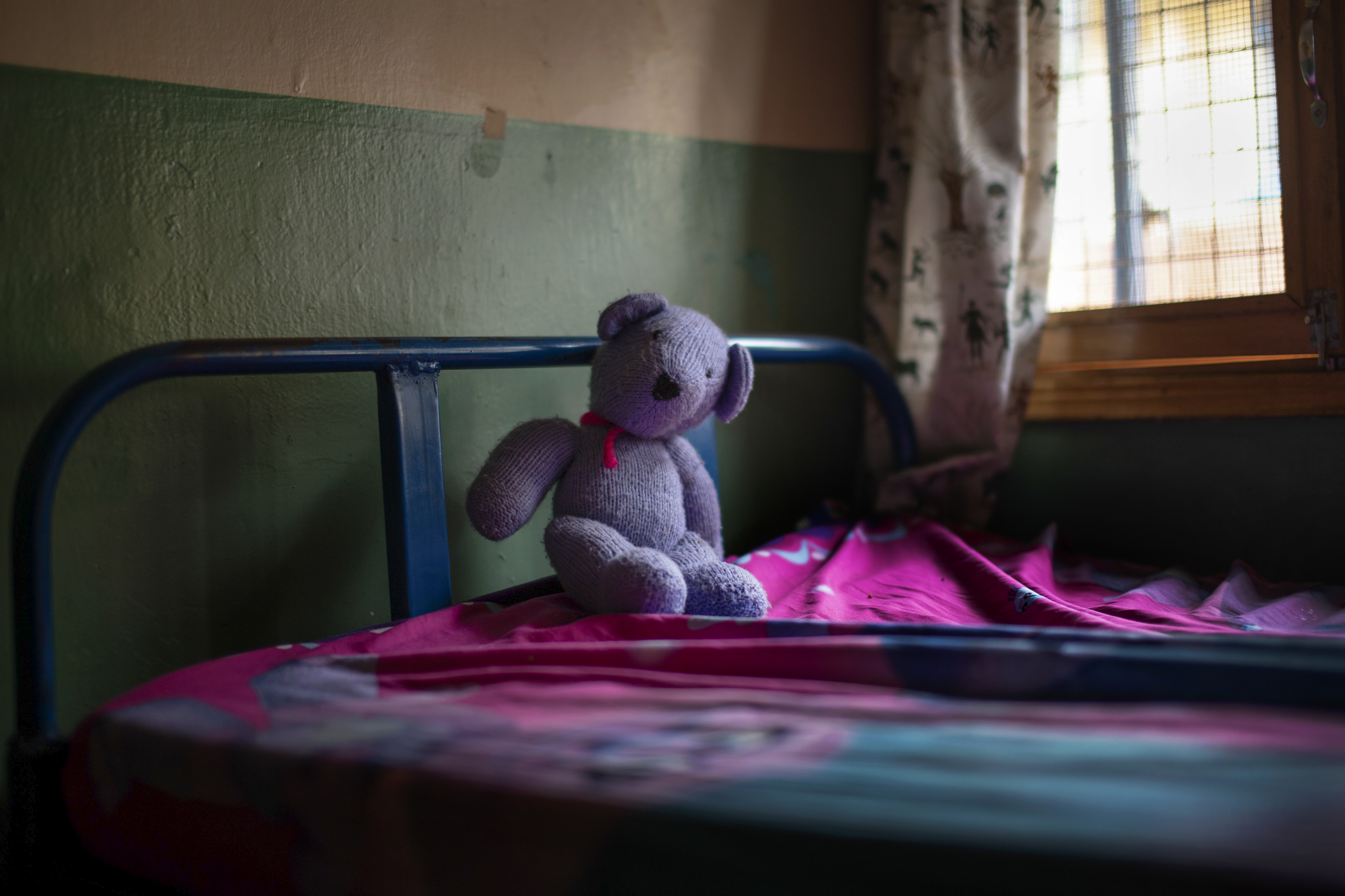 Bilde 1 viser Milly som sitter på sengen sin og smiler mens hun holder en bamse. Bilde 2 viser en annen bamse som ligger på sengen.