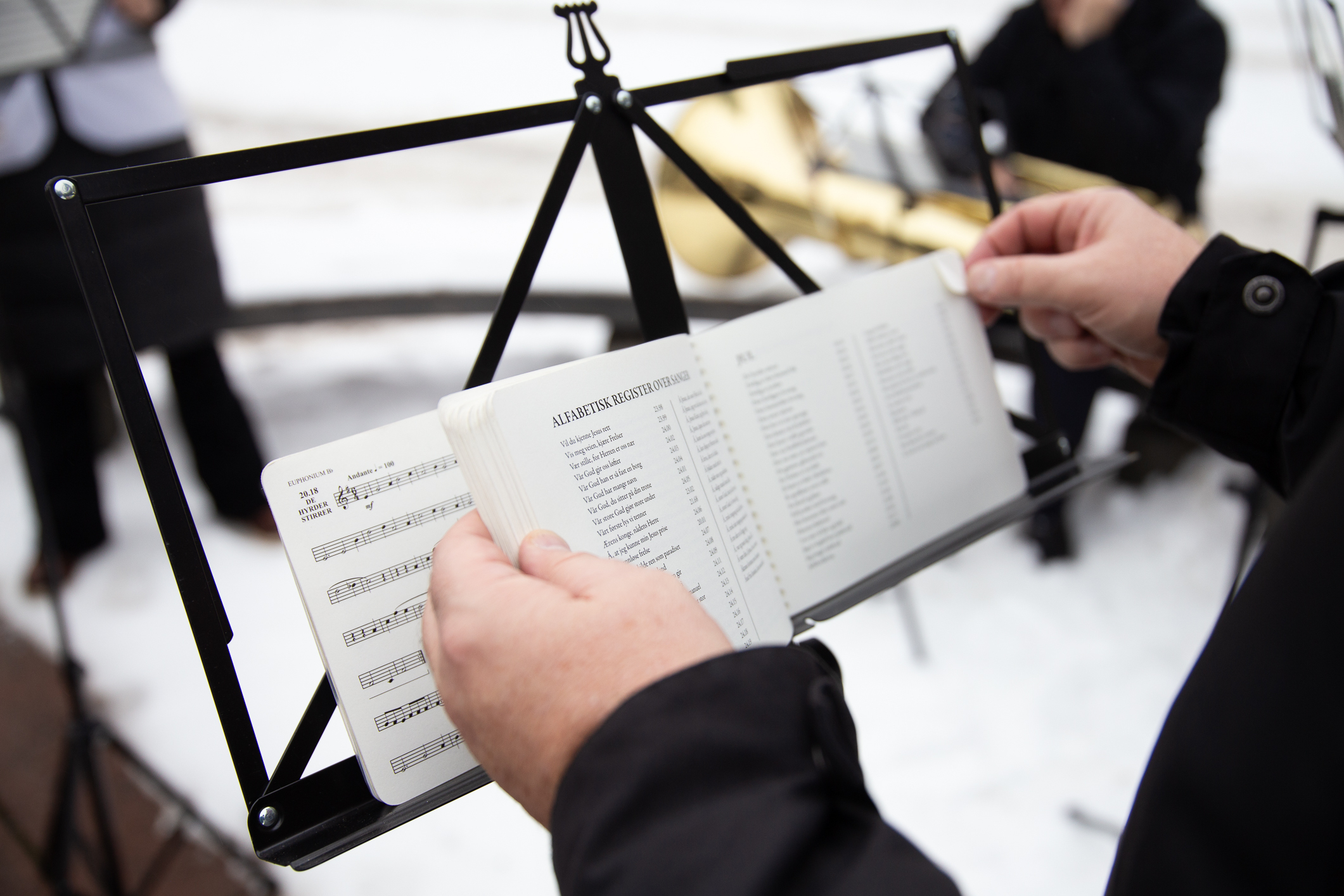 Notestativ med sangbok på. Hender som blar i den.