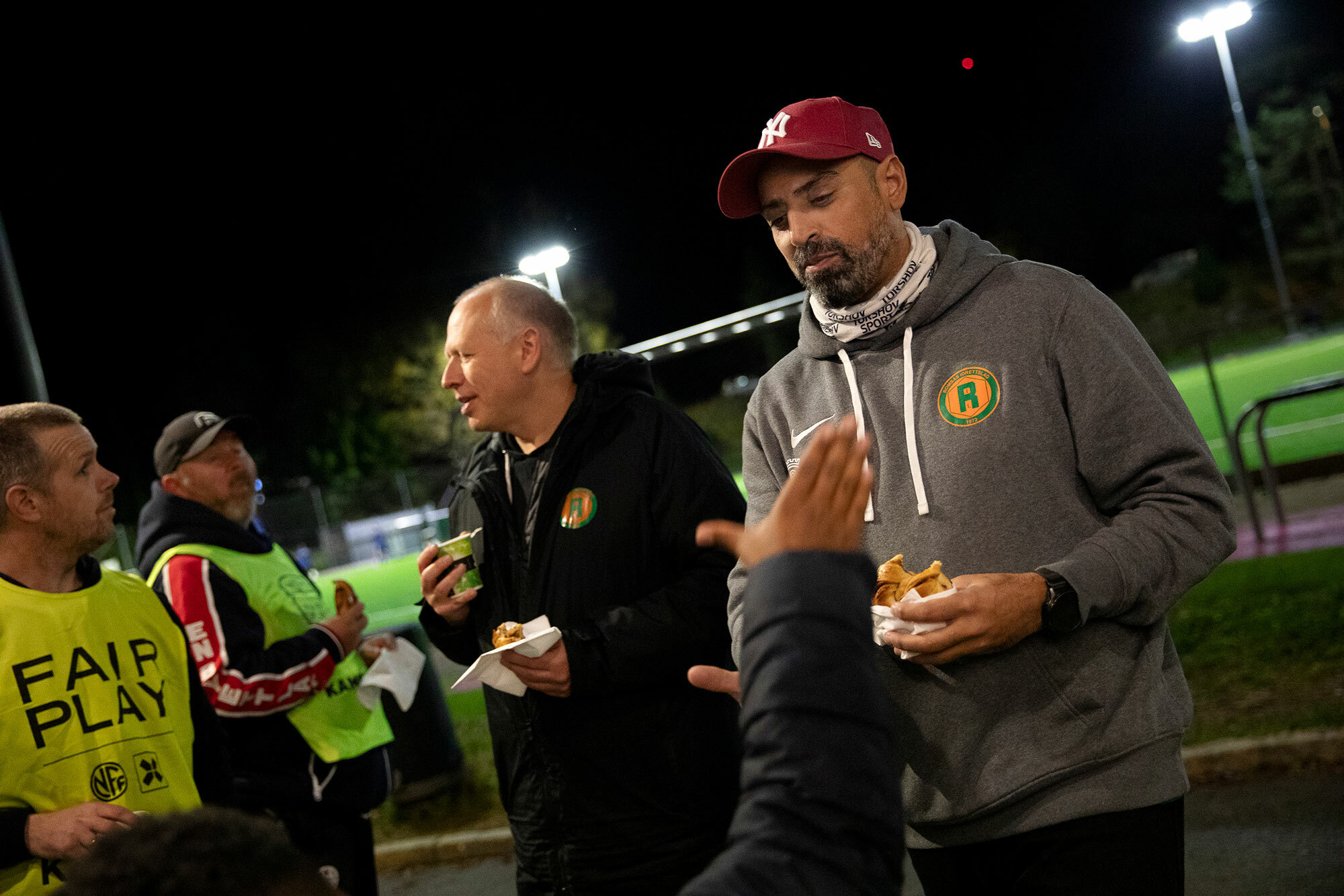 Foto: Mann i caps og hettegenser tar en high five med en barnehånd. Bak står flere andre voksne.