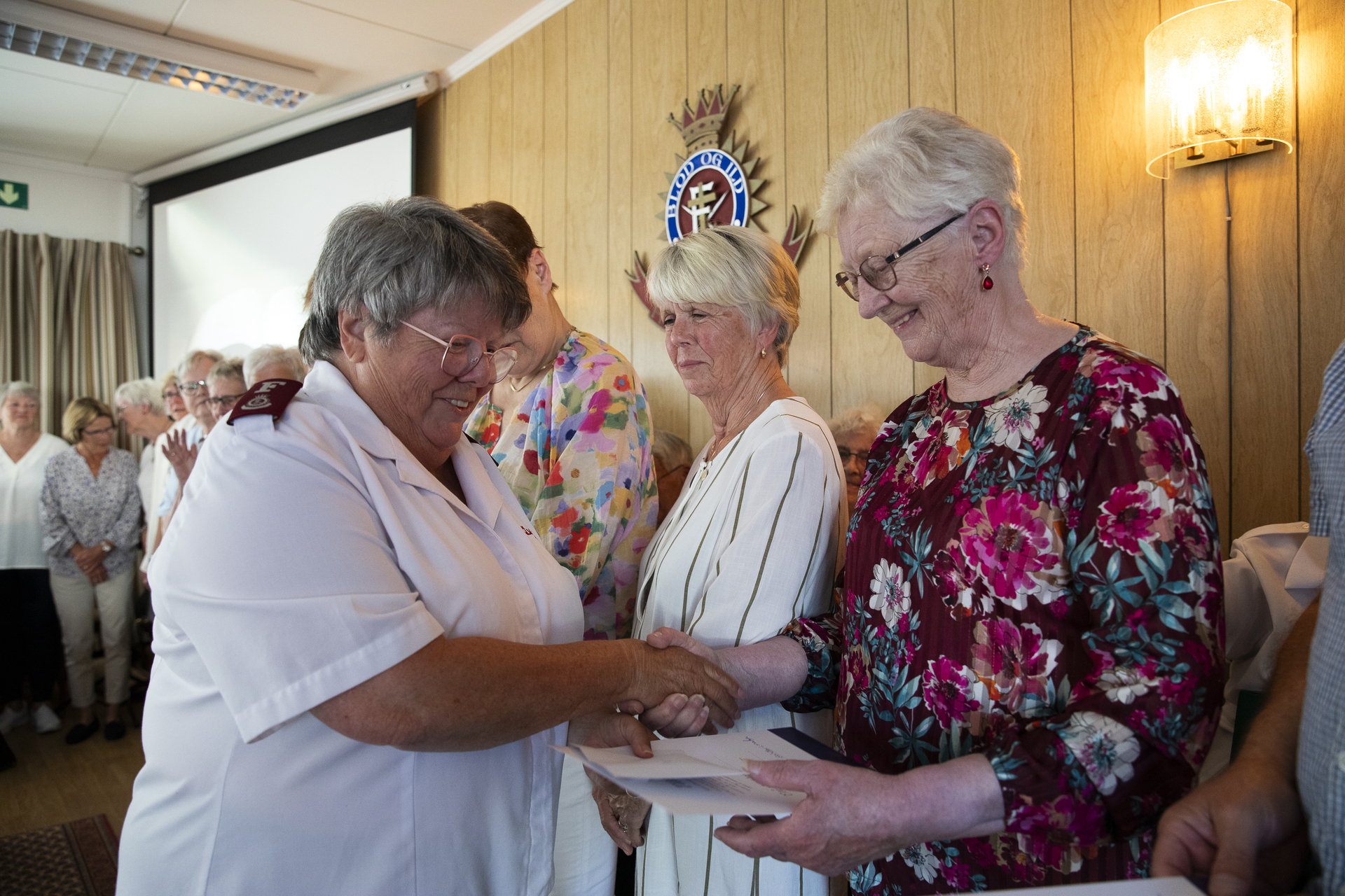 På et podium mottar en eldre kvinne, sammen med en rekke andre, et ark av en kvinne i FA-uniformsskjorte. Alle er i pentøy.