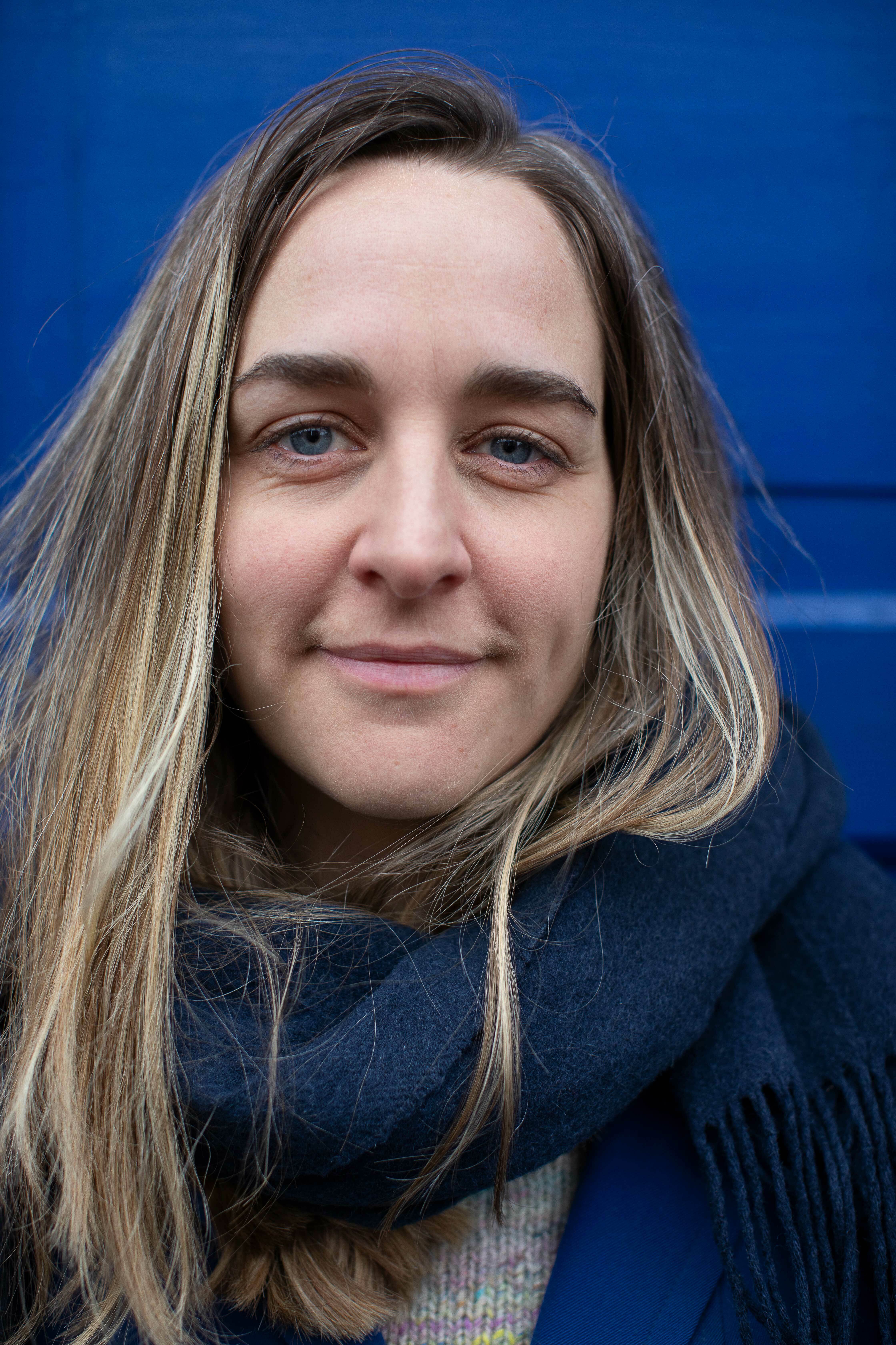 Kvinne med halvlangt hår og mørkt skjerf står lent mot en blå dør.