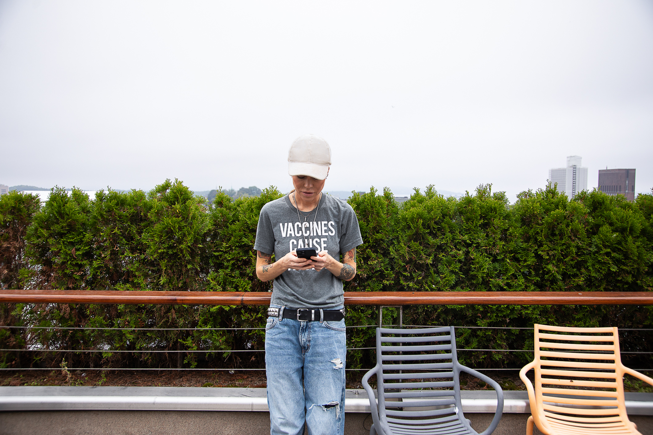 Kvinne som står på en terass ved siden av to solstoler og et rekkverk. Ser ned på mobilen sin.