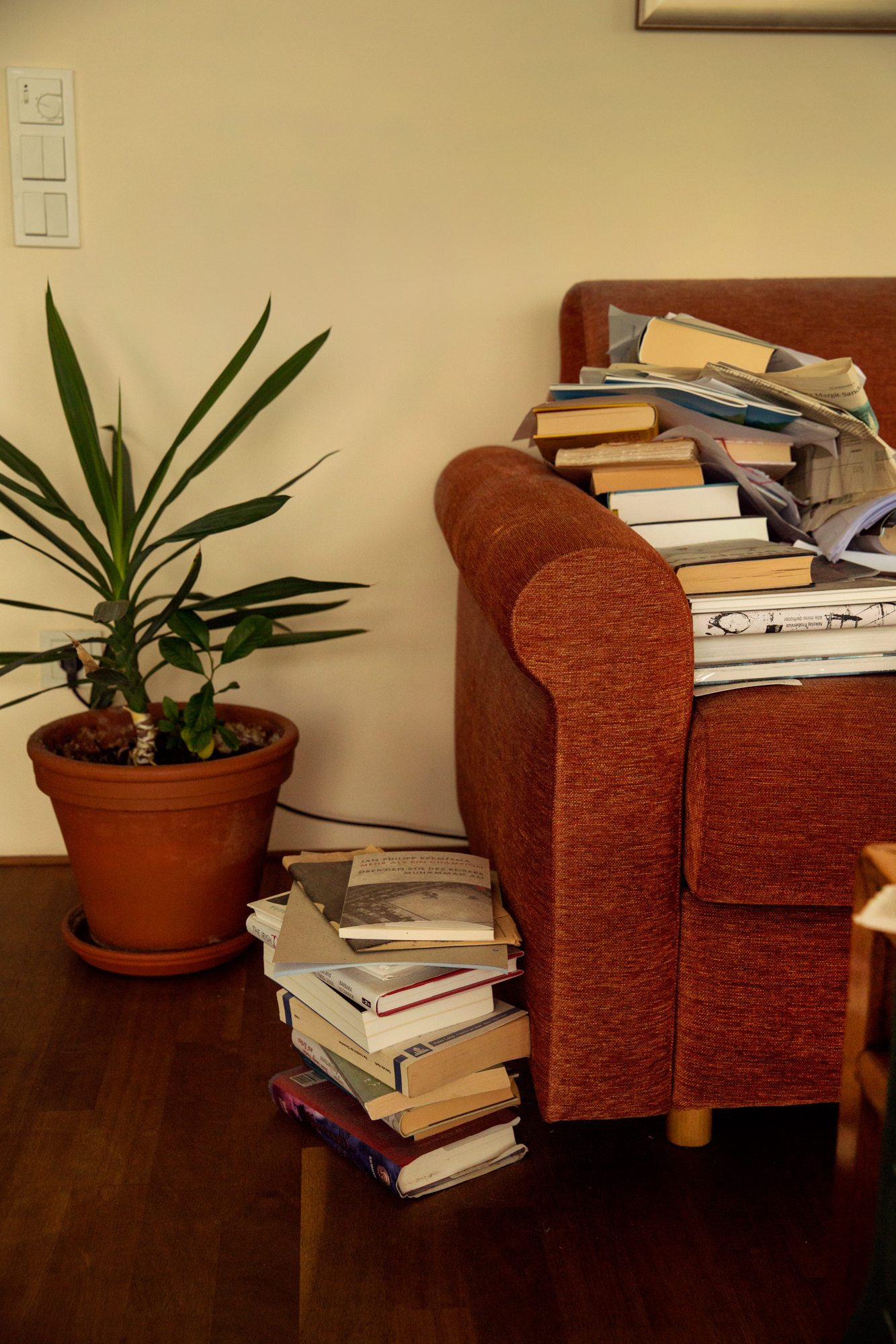 Foto: Rød sofa med mange  bøker opp og en stabel vd siden av.