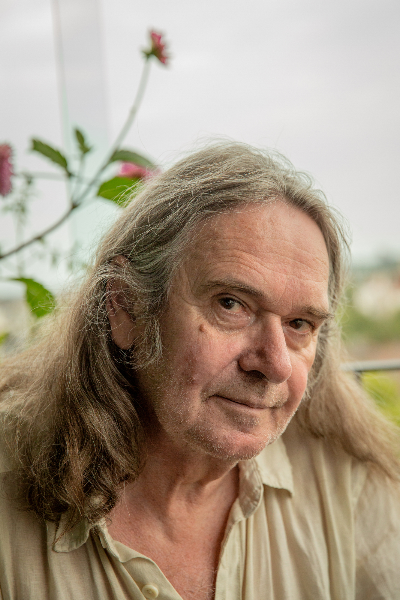 Foto: Mann med halvlangt hår sitter på balkongen med luft rundt og grønne planter bak.