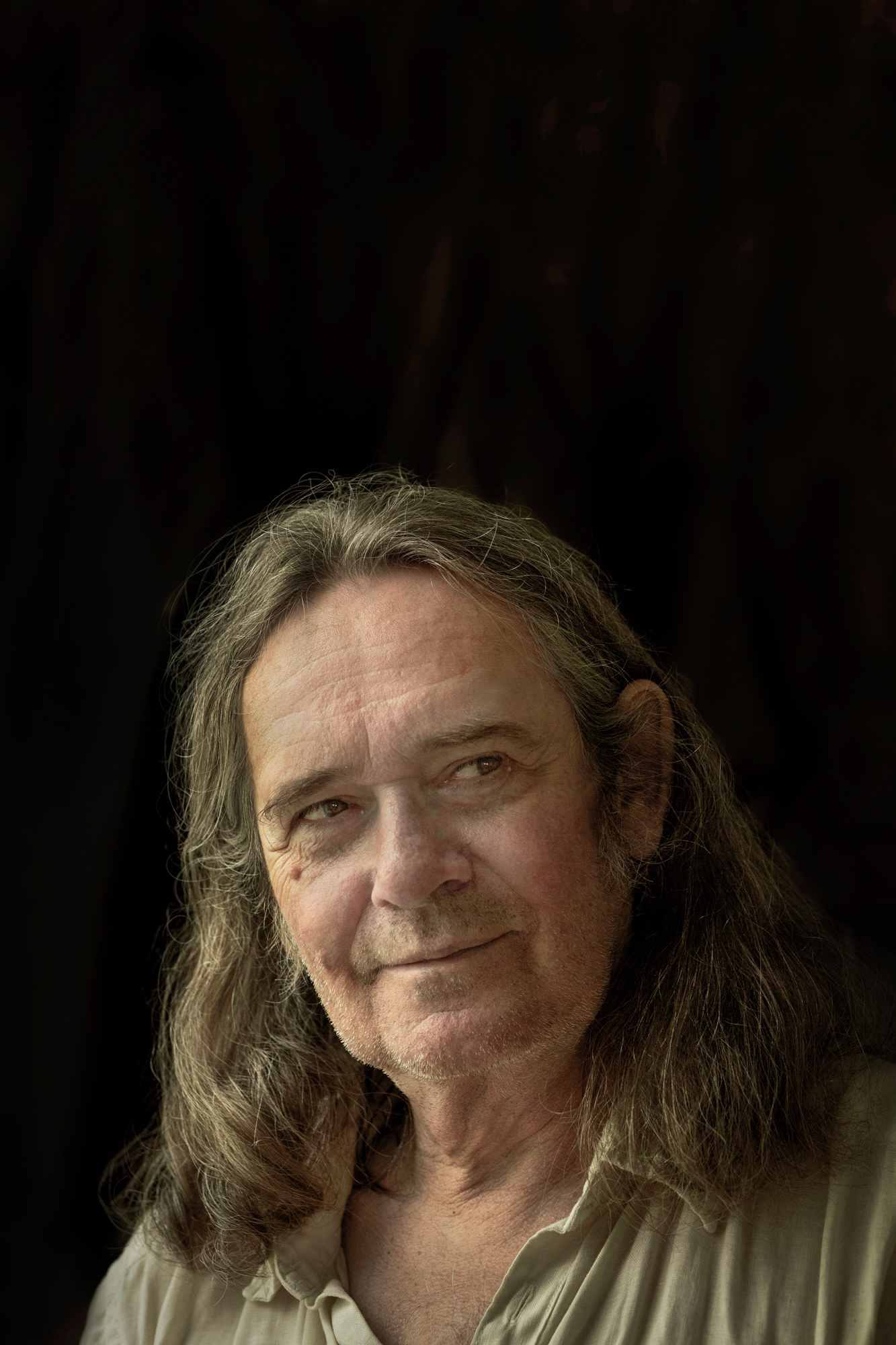 Foto: Mann med halvlangt, mørkt hår og beige skjorte fotografert med svart bakgrunn.