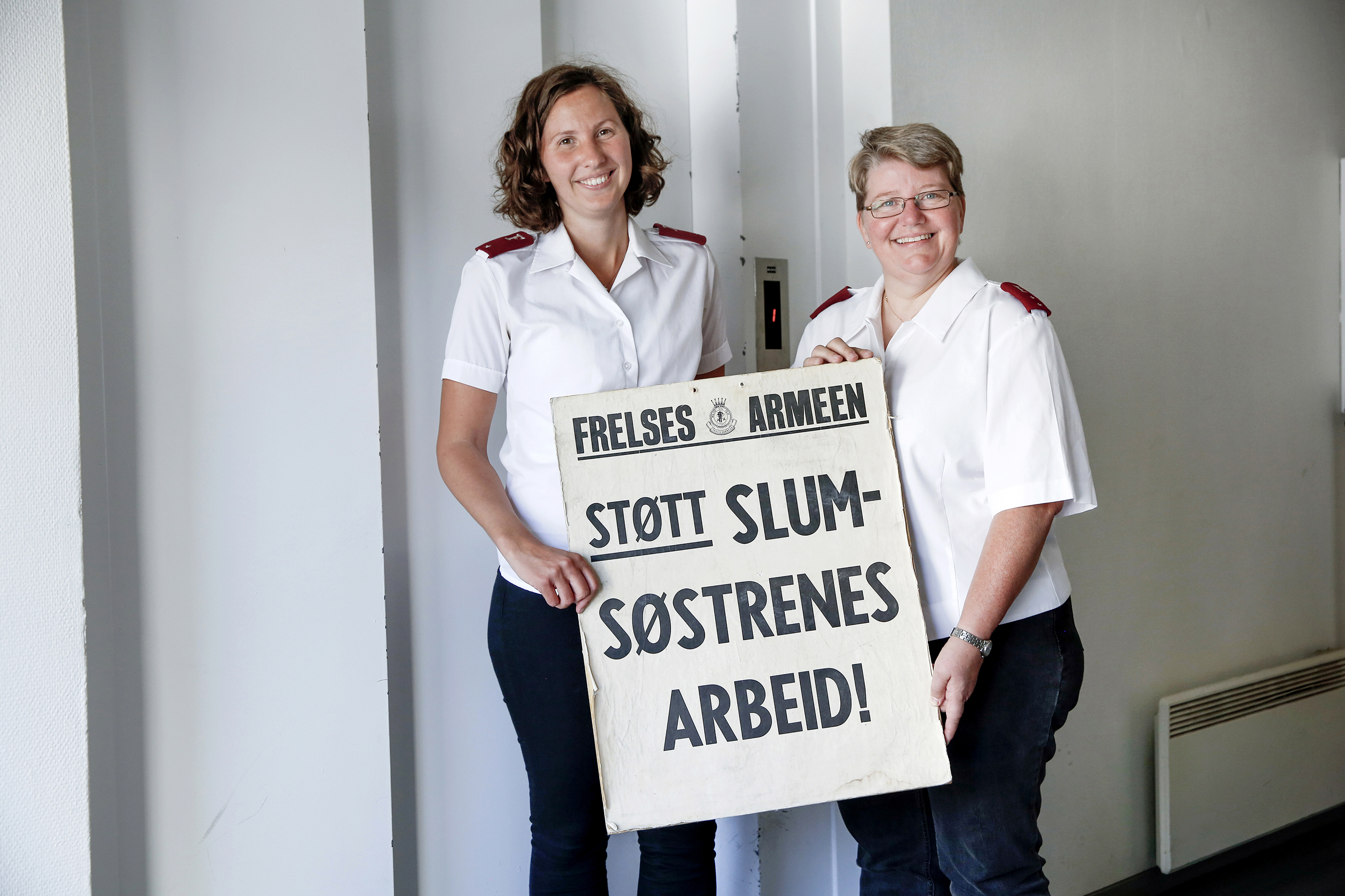 Tidligere slumsøster Monica Ellingsen og Irene Mathisen, begge i uniformer, holder en gammel innsamlingsplakat