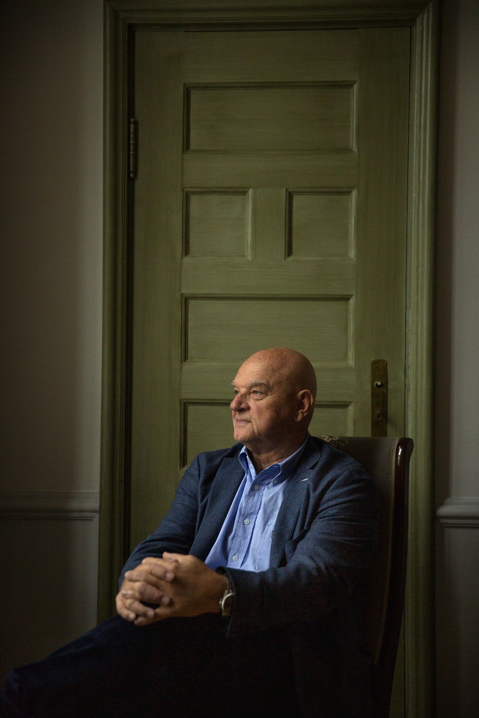 Bildet viser Johannessen som sitter på en stol foran en grønn dør. Han har hendene foldet rundt det ene kneet og ser ut mot siden.