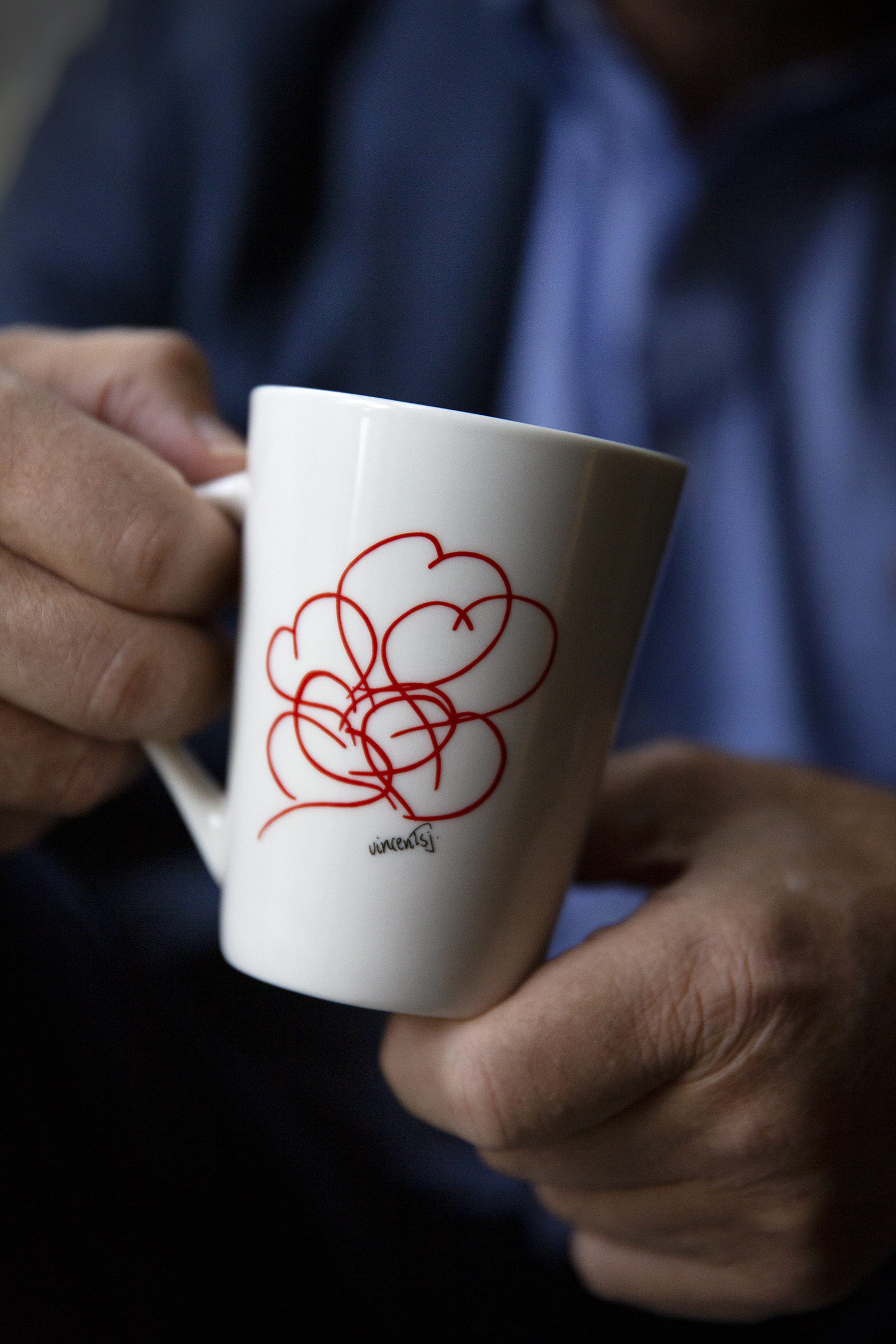 Bildet viser to hender som holder en hvit kopp med rødt motiv