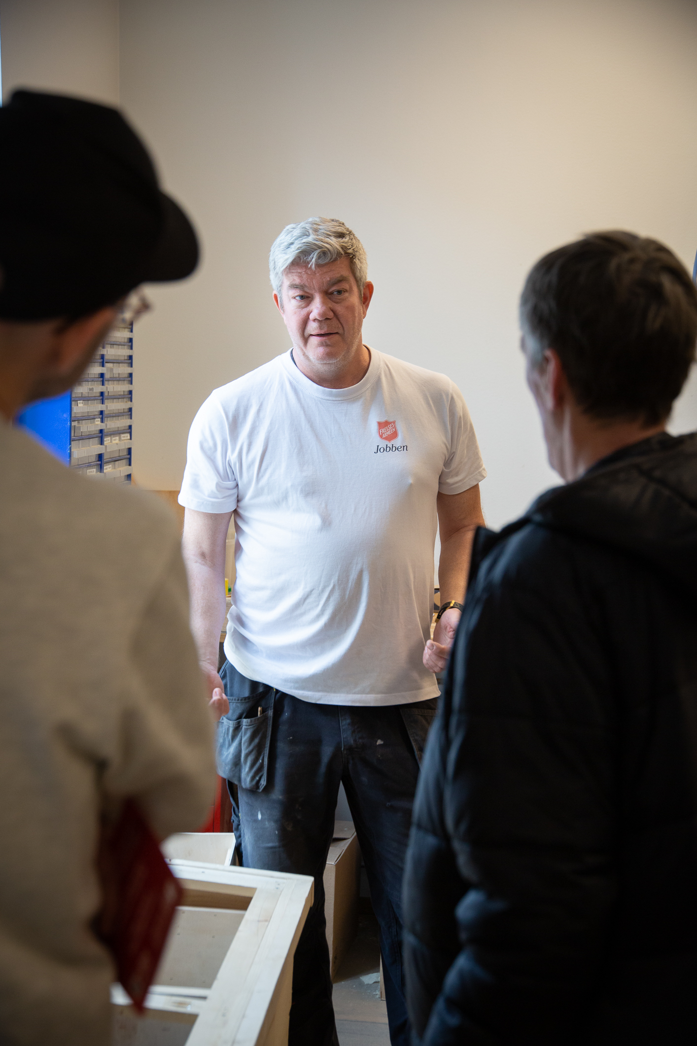 Tre menn snakker sammen inne i et snekkerverksted. To av dem med ryggen til.