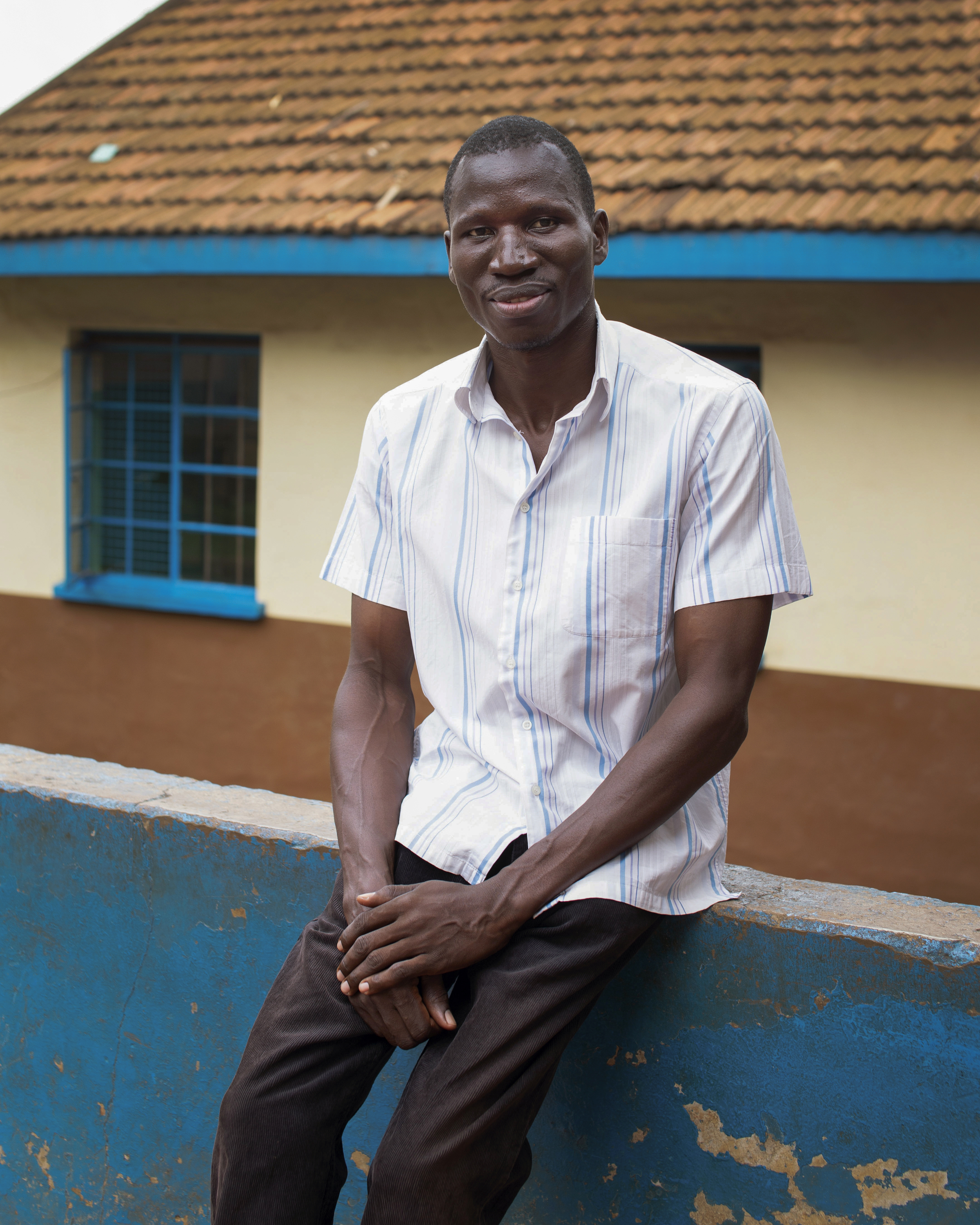 Bildet viser John som sitter utenfor barnehjemmet og ser i kamera.