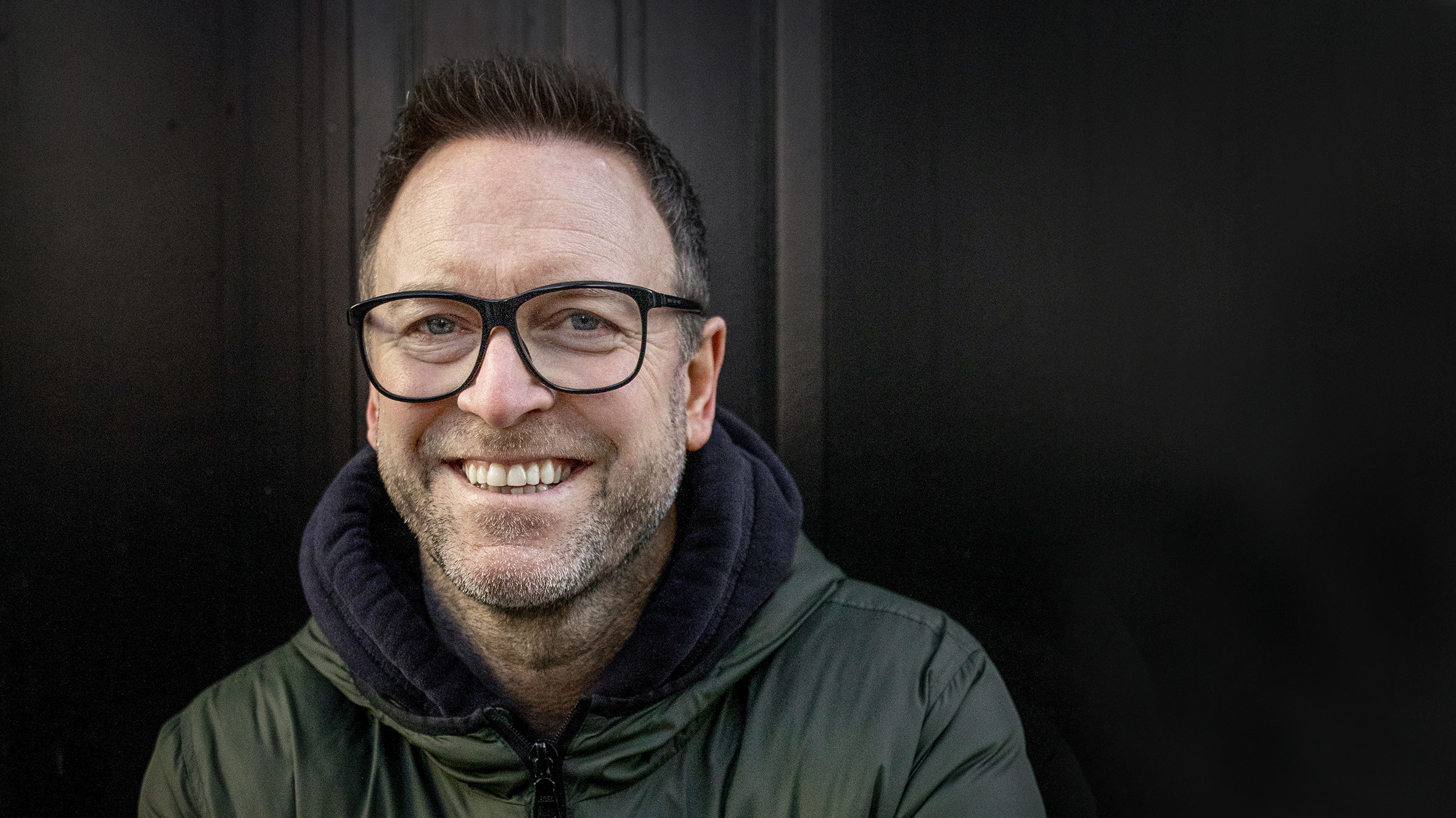 Nærportrett av Jonny Sjo som står foran en mørk ytterdør. Han smiler bredt til fotografen.