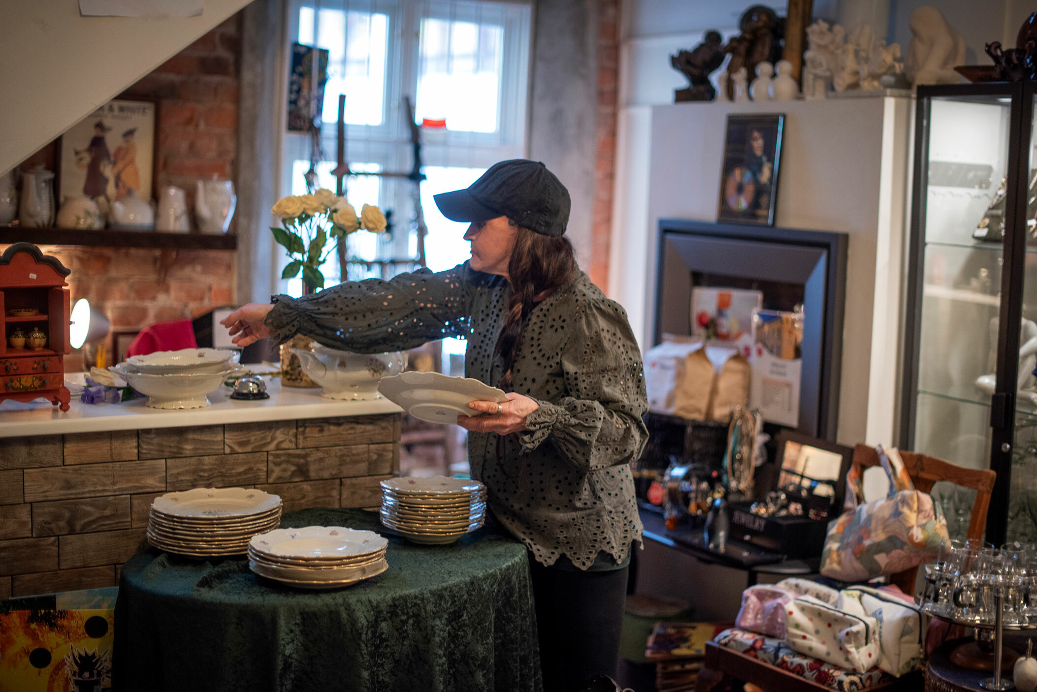 Foto: Kvinne i grønn bluse og svart caps rydder i en bruktbutikk.