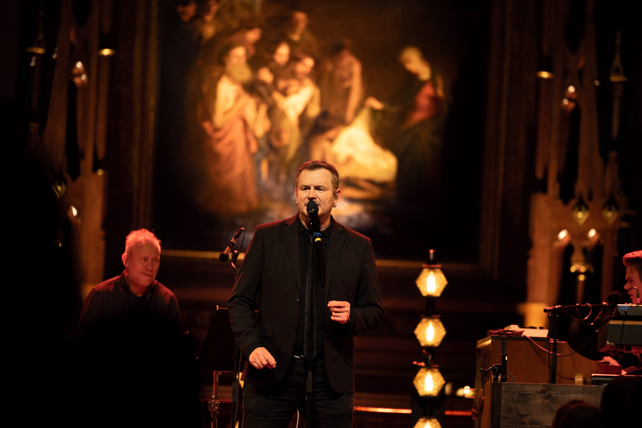 Foto: Mann i 30-årene står og synger foran en mikrofon i et kirkerom. Det er mørkt.