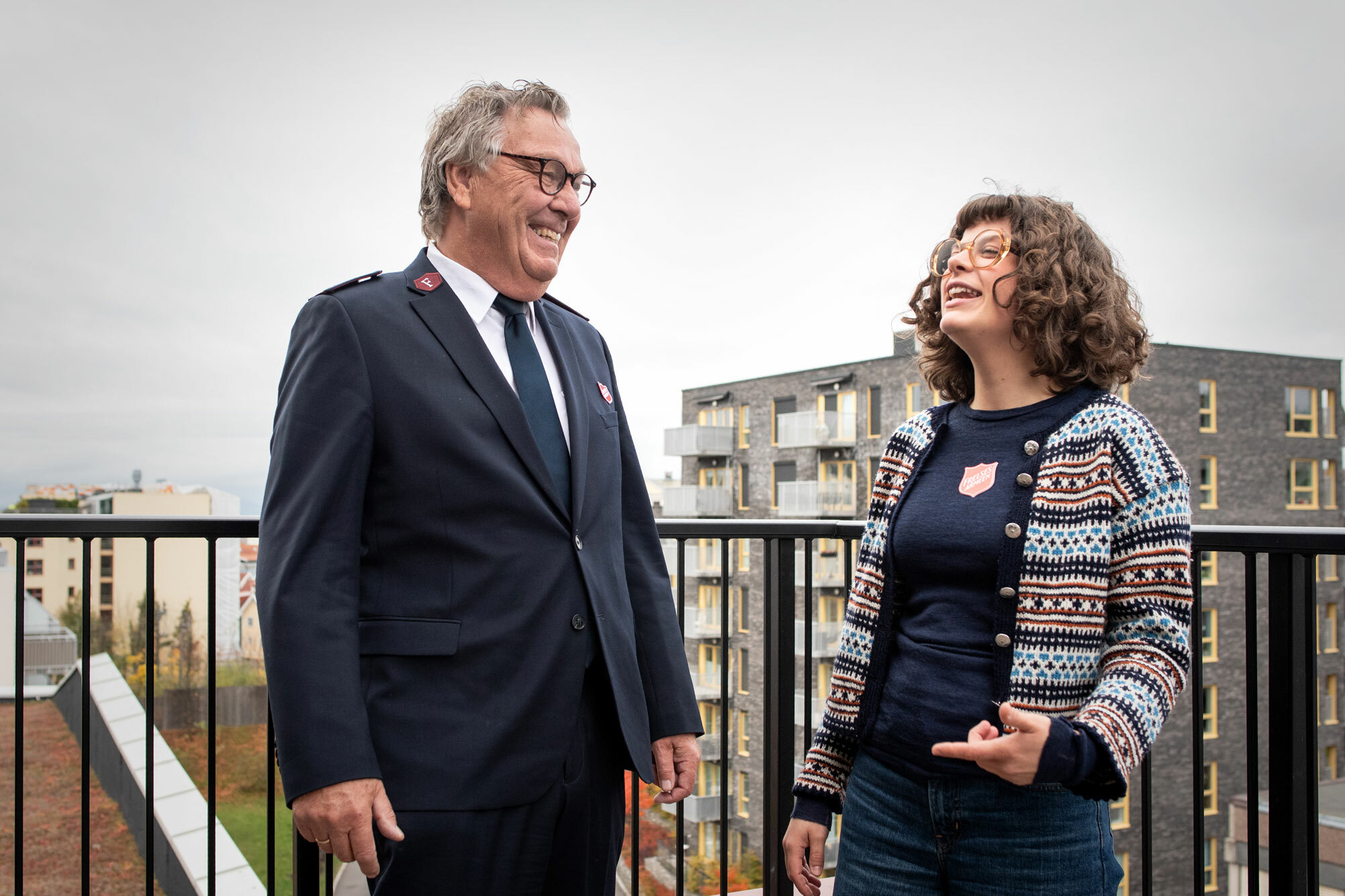 Foto: Eldre herre i uniform fra Frelsesarmeen står sammen med en ung jente med mørkt, krøllete hår. Begge har briller og står på en terrasse høyt hevet over Oslo.