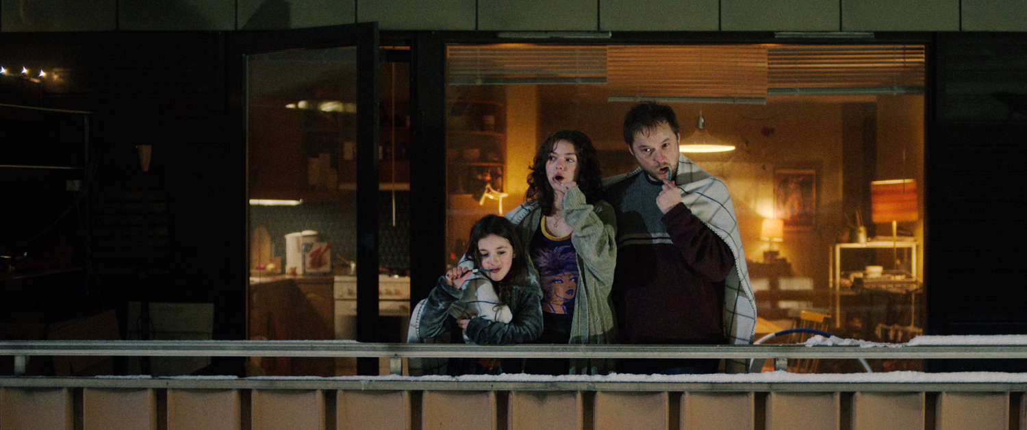 Foto: Filmscene i bredformat der far og to døtre står ute med tepper over seg. Det er kaldt og de pusser tennene.