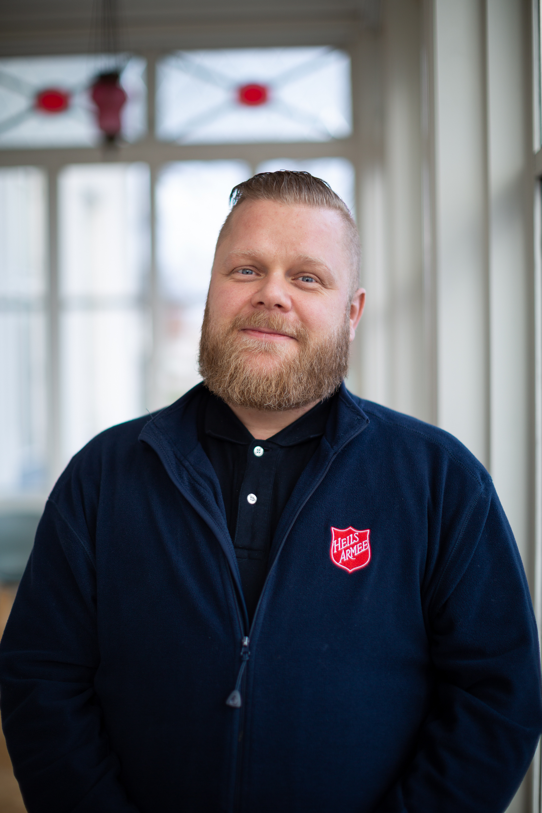 Kadett Sigurður Ívar Sölvason står på glassverandaen på Frelsesarmeens offiserskole på Jeløy. Han har på seg en  en mørkeblå genser med Frelsesarmee skjldet på brystet.