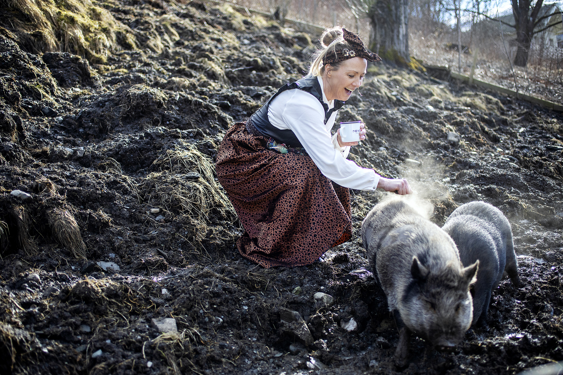 Kari Traa sitter på huk i selvsydd fantasibunad og klapper en gris