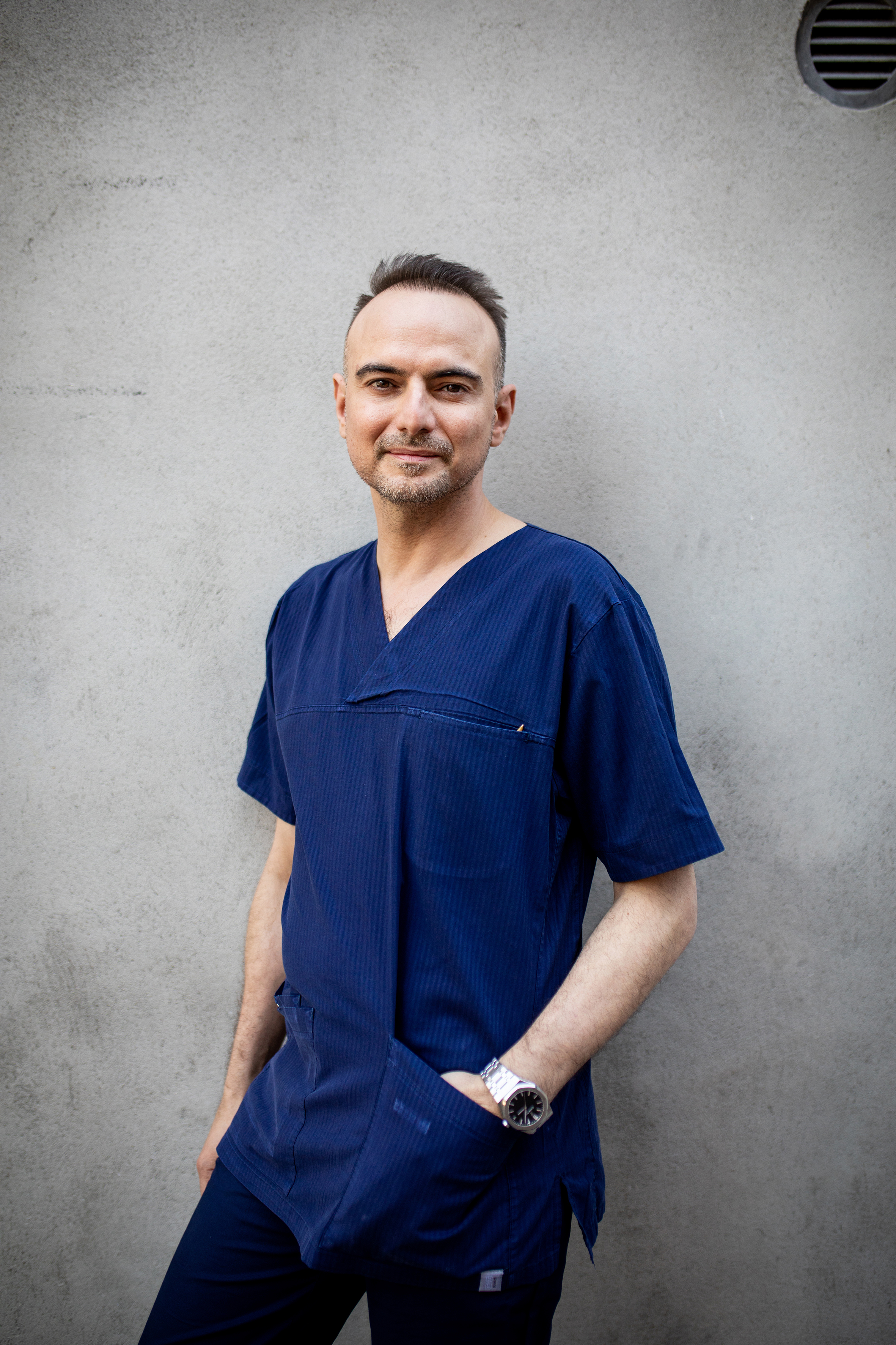 Karim Sayed, overlege ved Frelsesarmeens gatehospital i Oslo. Her står han i blå legeskjorte foran en grå murvegg.