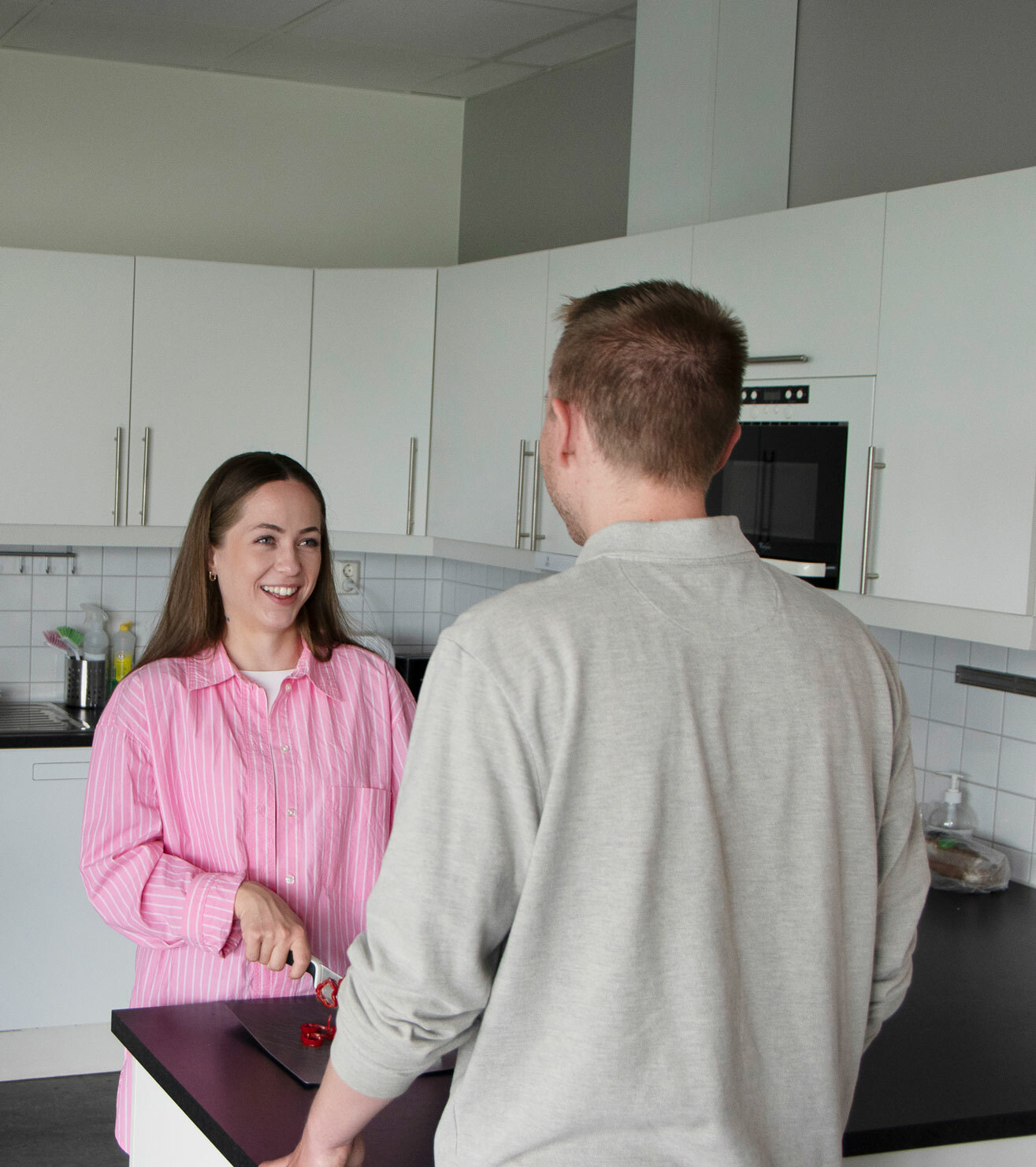 Foto: Kvinne med mørkt, langt hår i rosa skjorte står på et kjøkken og skjærer opp grønnsaker mens hun snakker med en ung gutt med ryggen til. Han har på seg en lys beige genser.