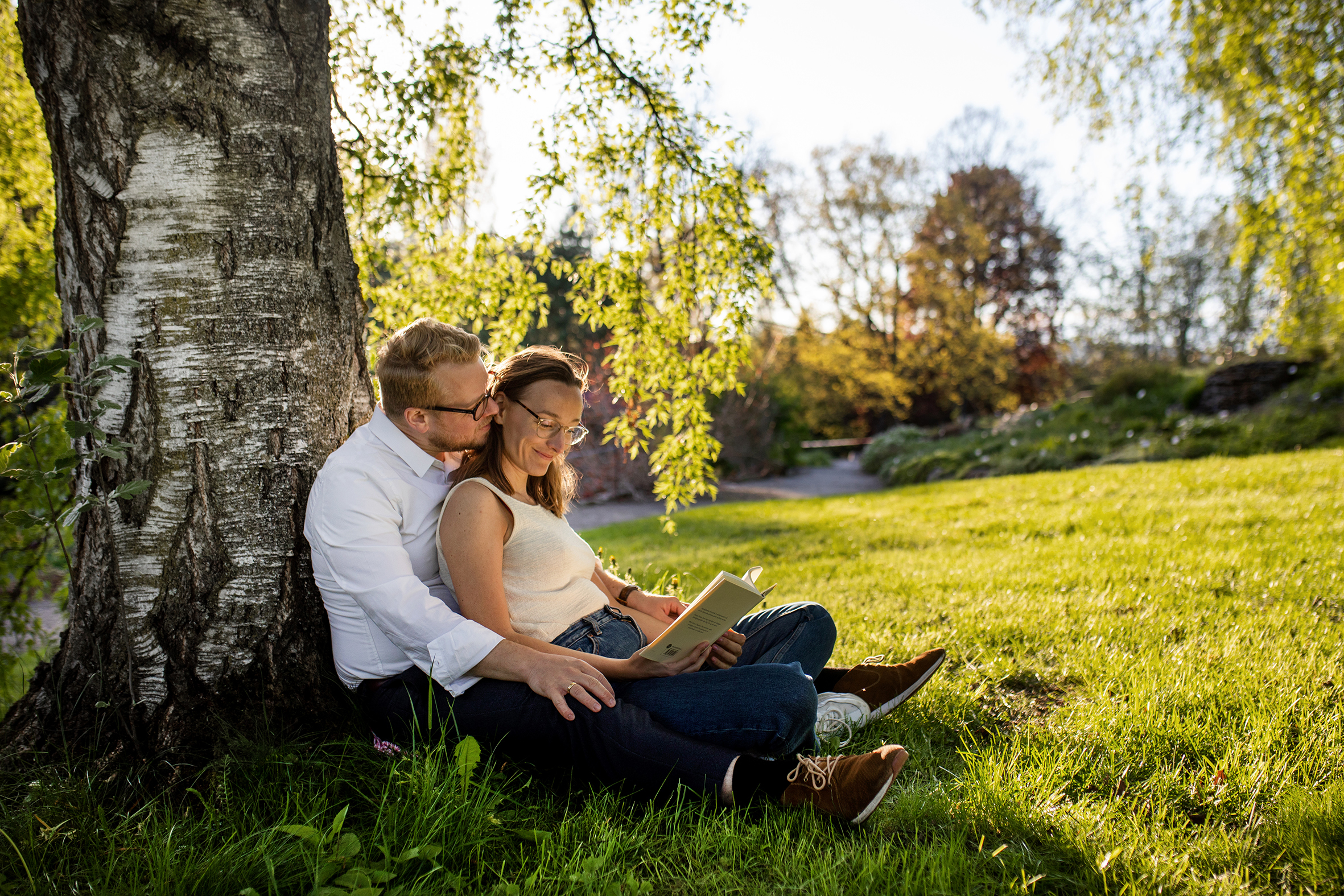 En ung dame og mann sitter under et tre og leser en bok sammen