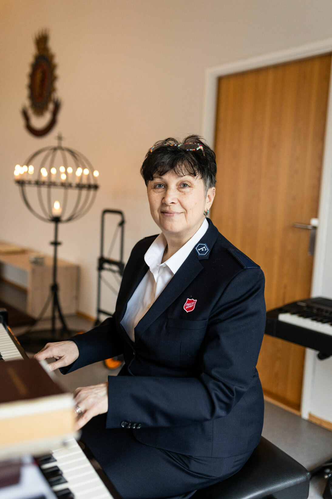 Foto: Kvinne i 60-årene sitter foran et piano. På seg har hun en uniform fra Frelsesarmeen.