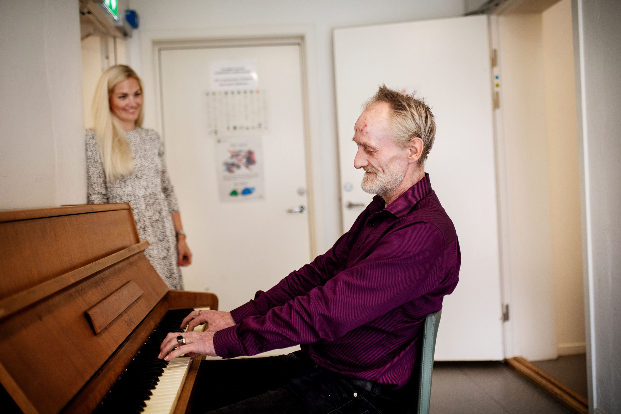 Beboer Knut spiller på Piano og daglig leder Silje hører smilende på
