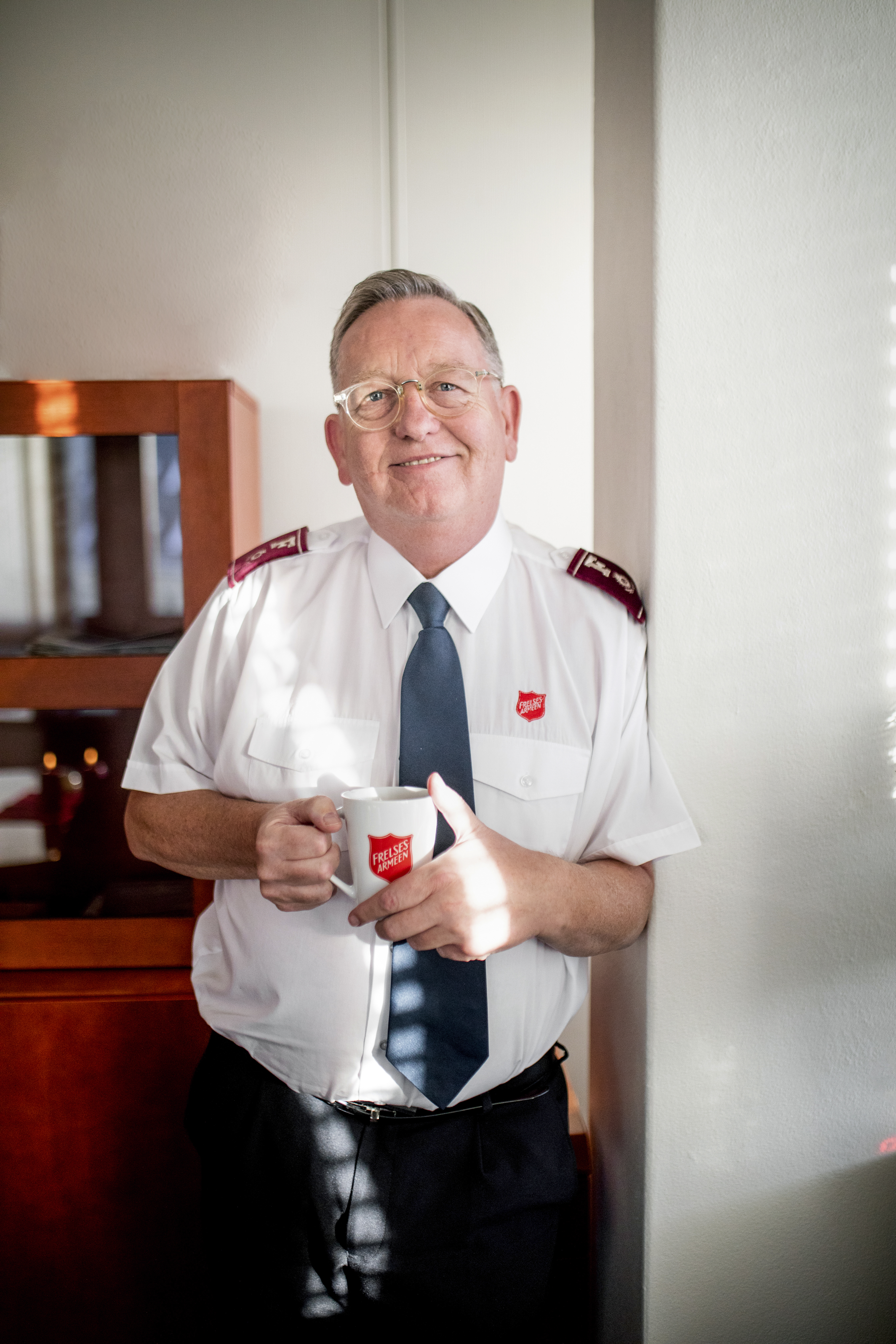 tidligere toppleder i Frelsesarmeen, William Cochrane, står iført uniformsskjorte med et kaffekrus i hendene og ser inn i kameraet.