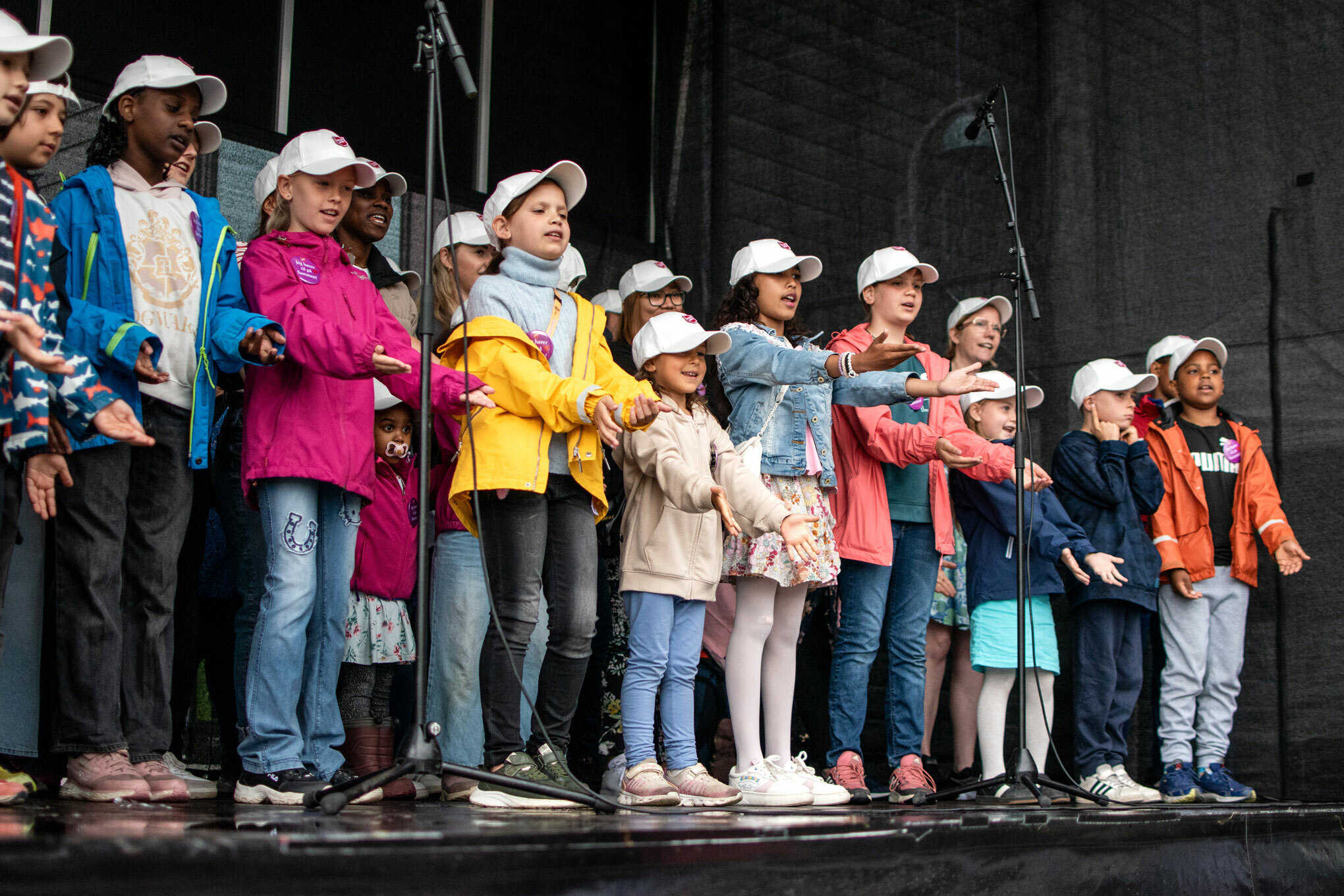 Foto: Barnekor i fargerike klær synger fra en scene. De er i 10-12-årsalderen.