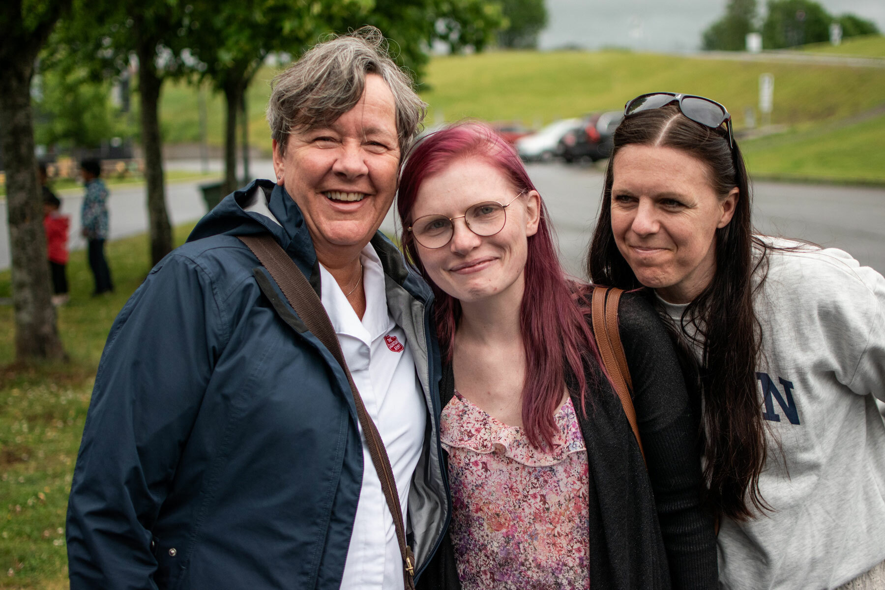 Foto: Tre kvinner i 40-50 årene med kort gråblondt hår, burgunder-farget hår og mørkt hår. De står tett utenfor. Den første har en hvit skjorte med rød logo fra Frelsesarmeen på.