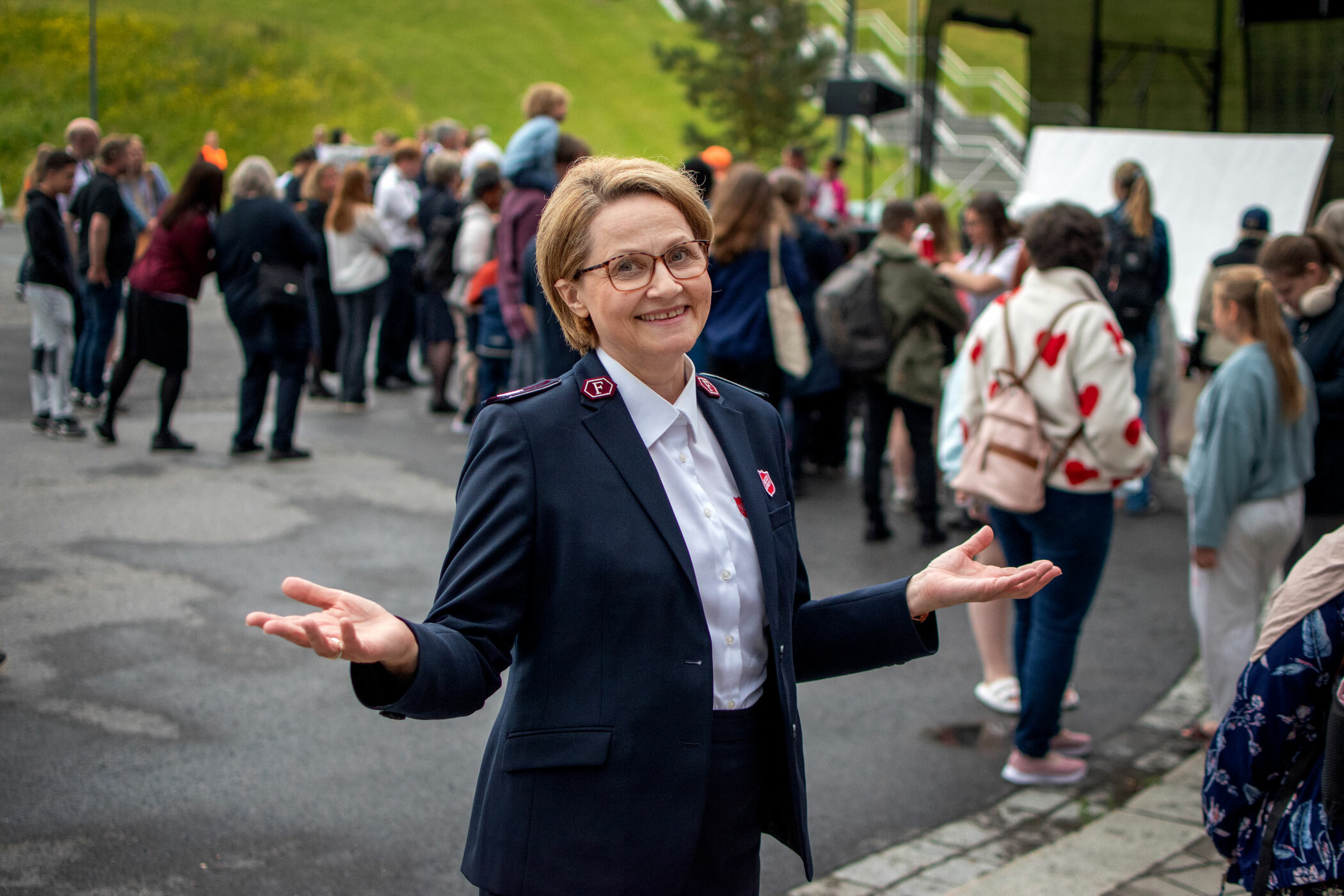Foto: Kvinne i 60-årene med bob-klipp og briller. Hun har på seg uniform fra Frelsesarmeen og holder ut hendene.