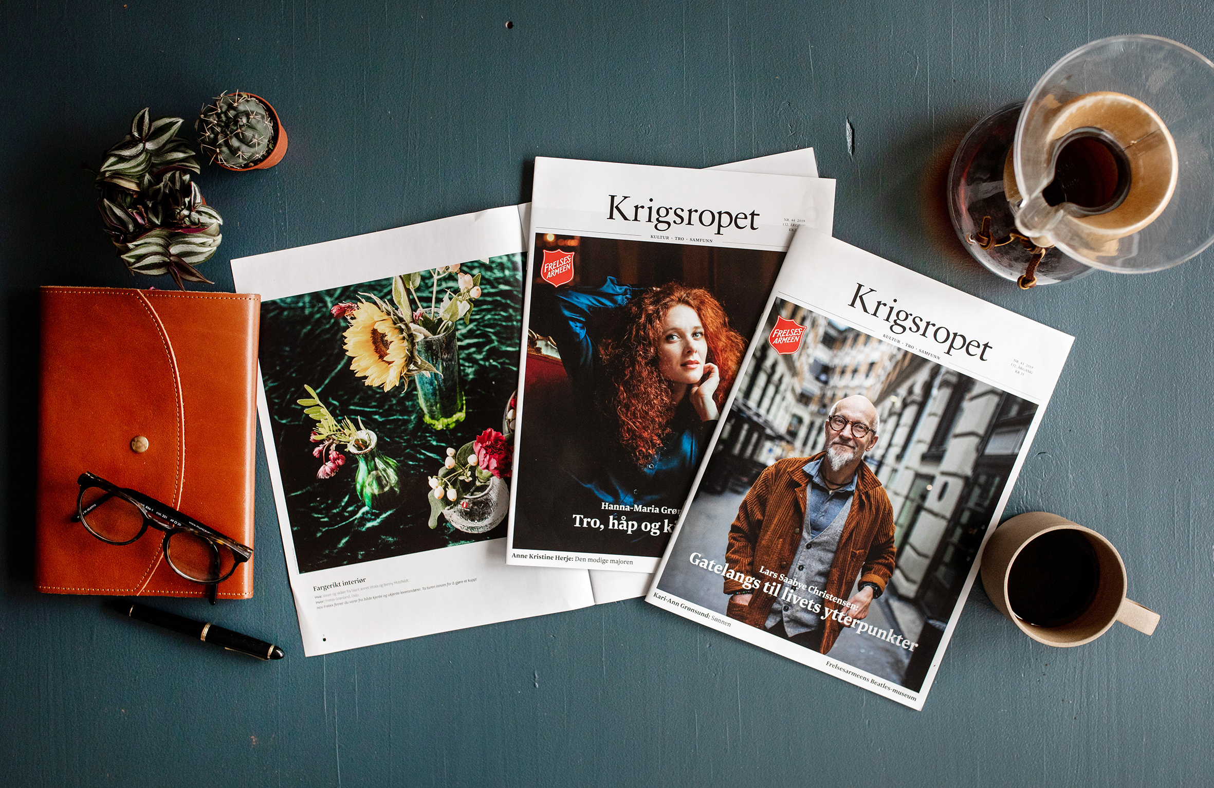 Bilde på sjøgrønn bakgrunn. Kaffe og bøker ligger i ytterkanten av bildet. Hovedfokus er på forsidene av tre utgaver av Krigsropet.