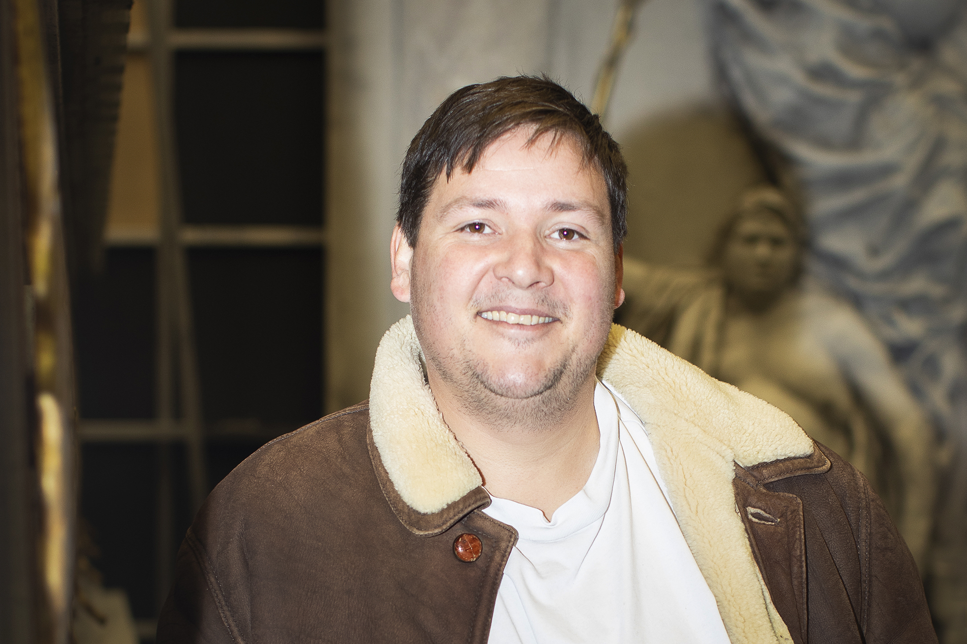 Mann i skinnjakke. Nærbilde med "marmorstatuer" i bakgrunnen.