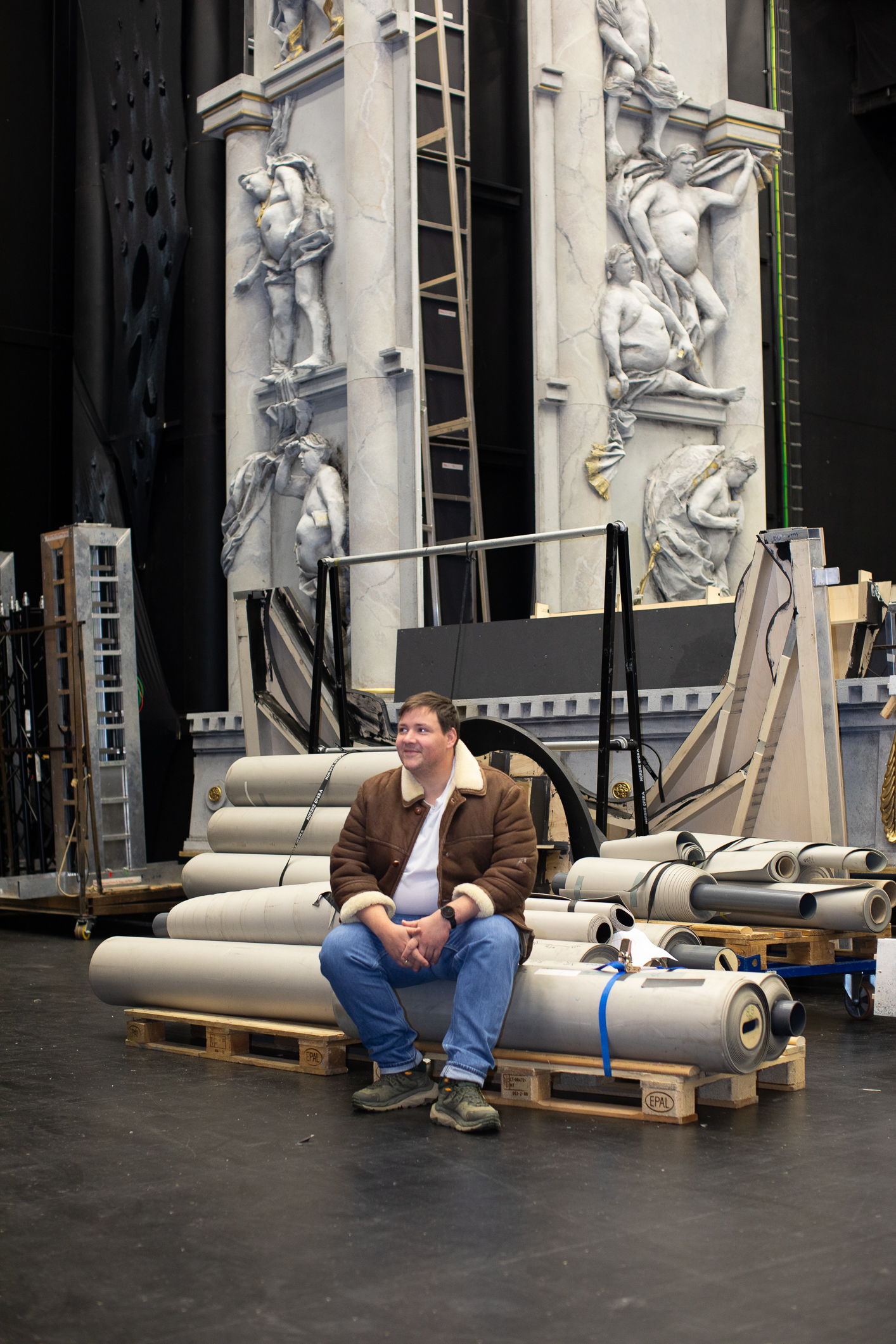 Mann i skinnjakke sitter ved foten av høyreiste marmorstatuer.