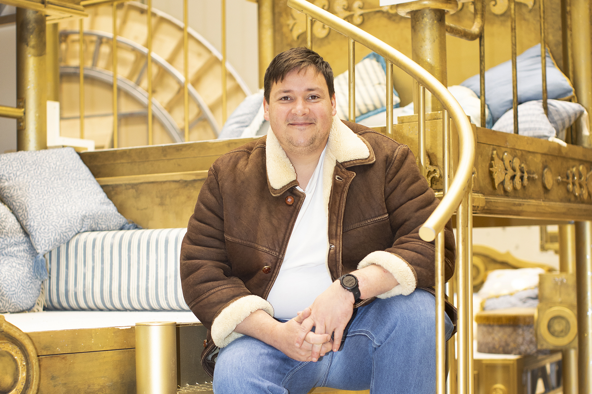 Mann i skinnjakke sitter i en forgylt trapp på en scene.