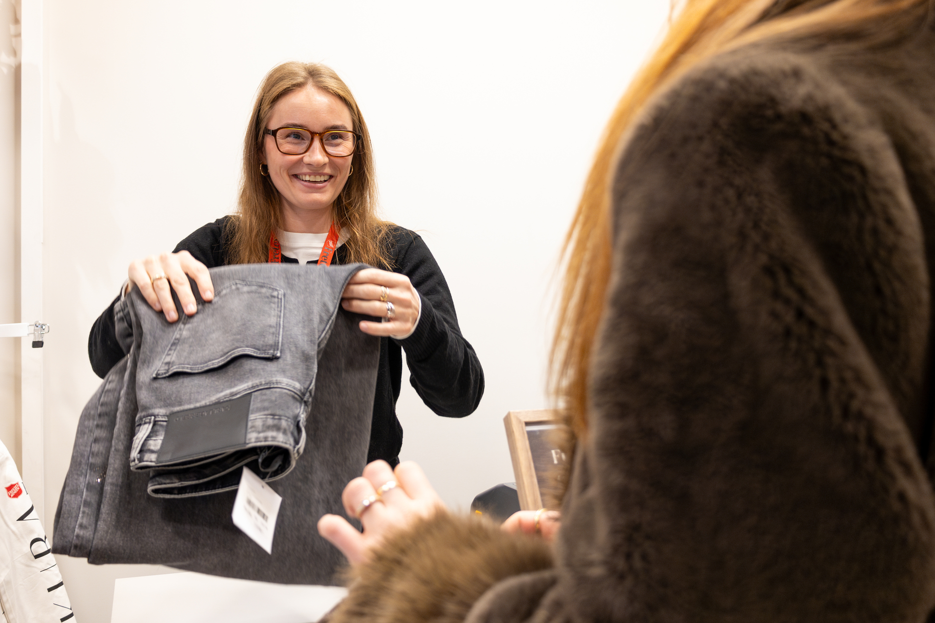 Foto: To bilder etter hverandre, der det første er av to venninner i 20-årene. Hun ene har svart hår, hun andre rødt. På det neste bildet betaler hun med rødt hår for en grå bukse. Ung dame med briller ekspederer henne.