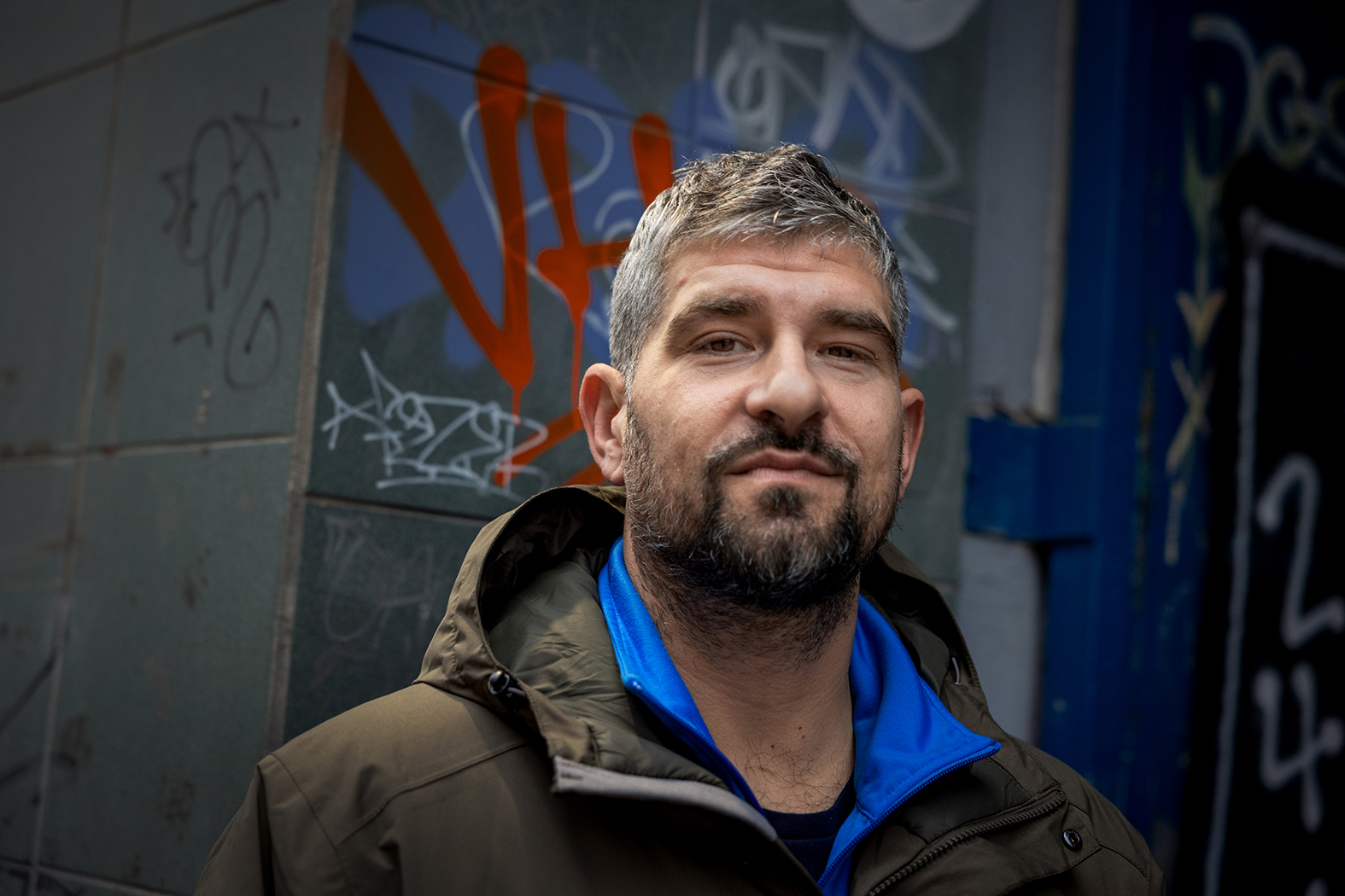 Foto: Programleder Leo Ajkic, en mann med grålig hår og skjegg ser i kamera. Han står ute, foran en vegg full av grafitti.