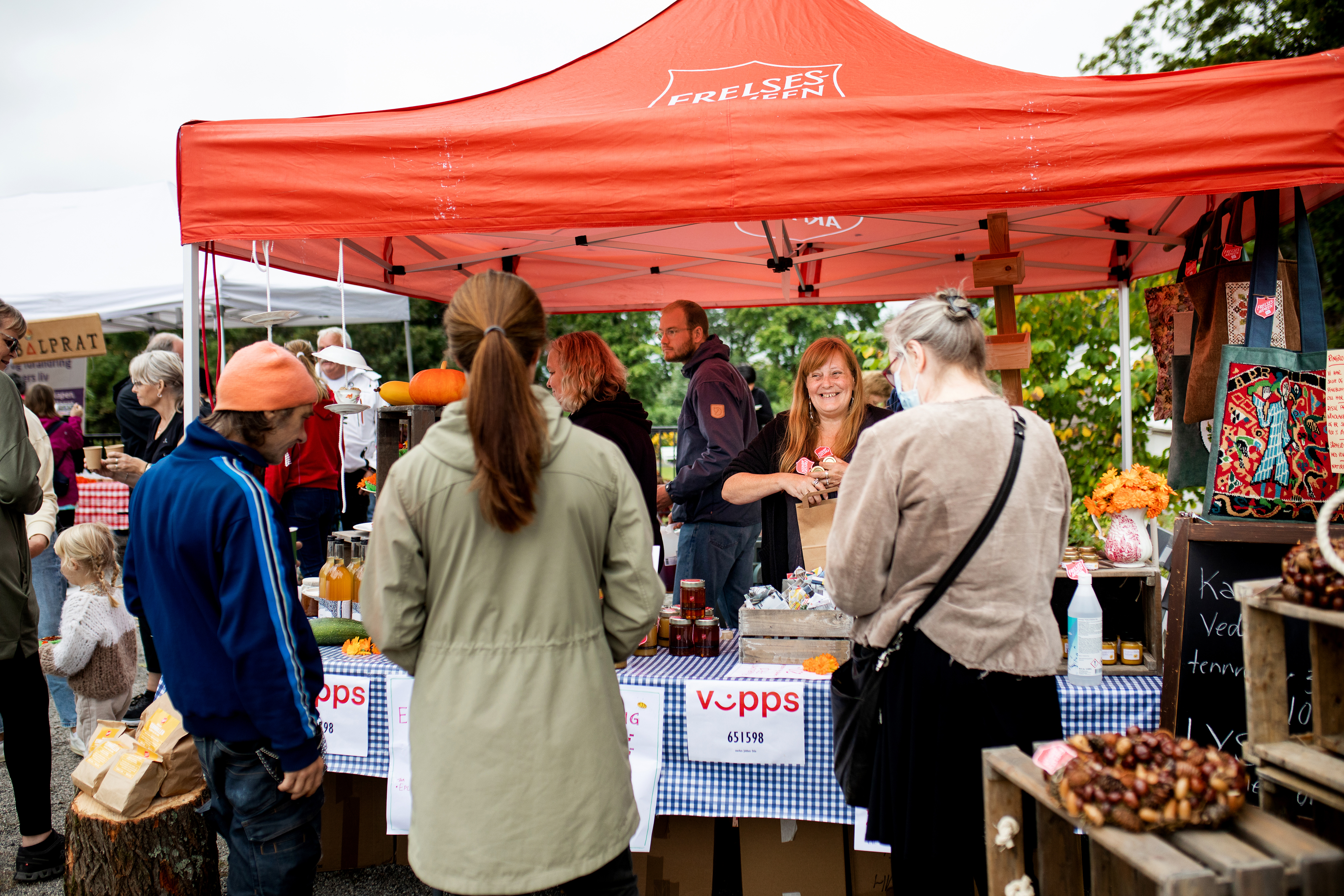 Deltager Lillo pakker ned noen glass med ringblomstsalver i en papirpose og overrekker den smilende til en kunde.